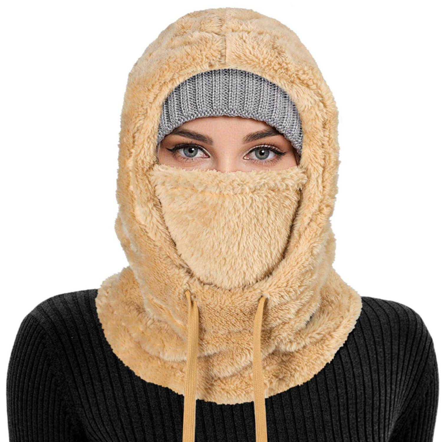 Person trägt eine beige pelzige Sturmhaube und eine graue Beanie, wobei nur die Augen sichtbar sind, vor weißem Hintergrund.