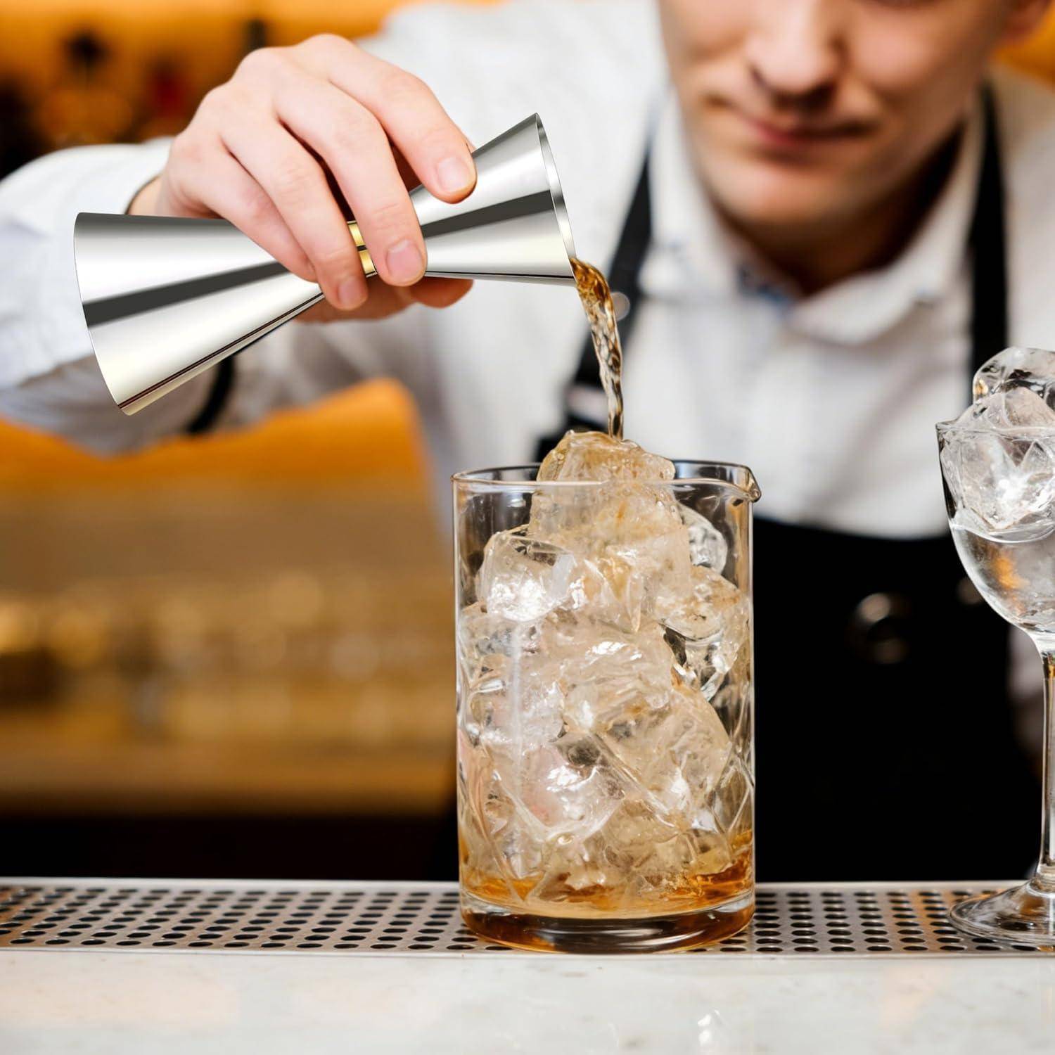 Ein Barkeeper gießt ein Getränk aus einem Metall-Jigger in ein Glas, das mit Eis gefüllt ist, auf einem Tresen.
