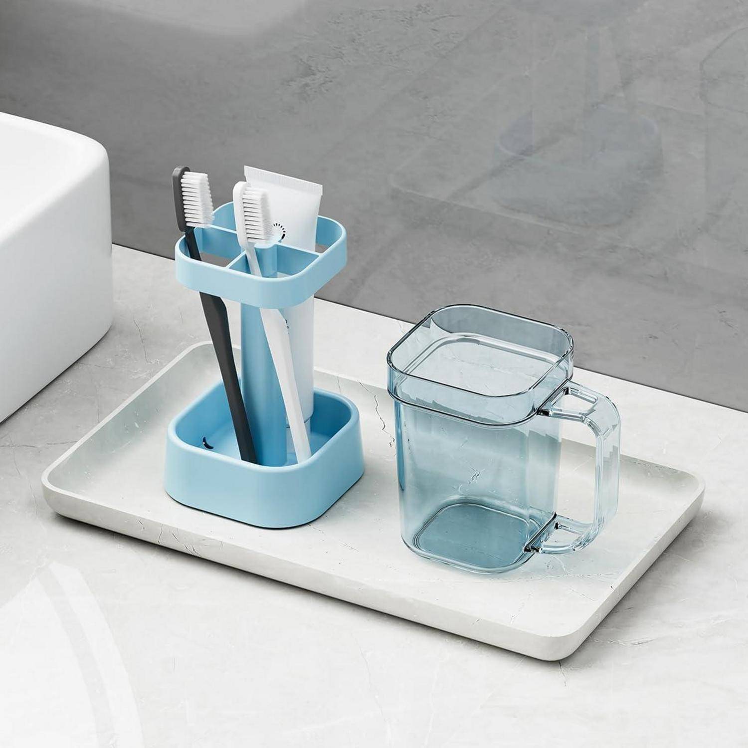 Badezimmer-Tablett mit einem Zahnbürstenhalter, der drei Zahnbürsten enthält, und einer durchscheinenden blauen Tasse oder einem Becher neben einem Waschbecken.