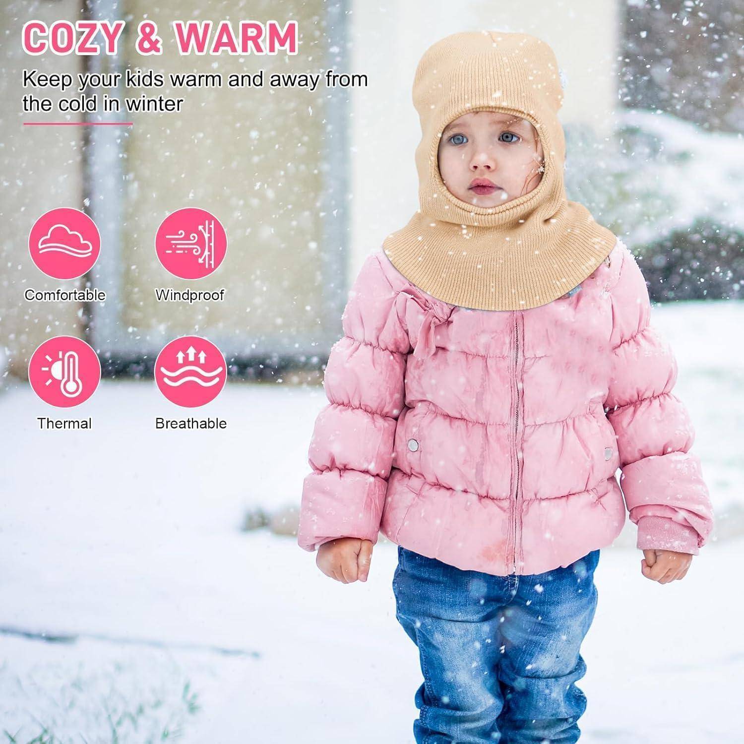 Kleines Kind in rosa Winterjacke und beigem Sturmhaube, das im fallenden Schnee steht, wirbt für "COZY & WARM"" Kinder-Winterkleidung, die bequem, winddicht, wärmewirksam und atmungsaktiv ist.