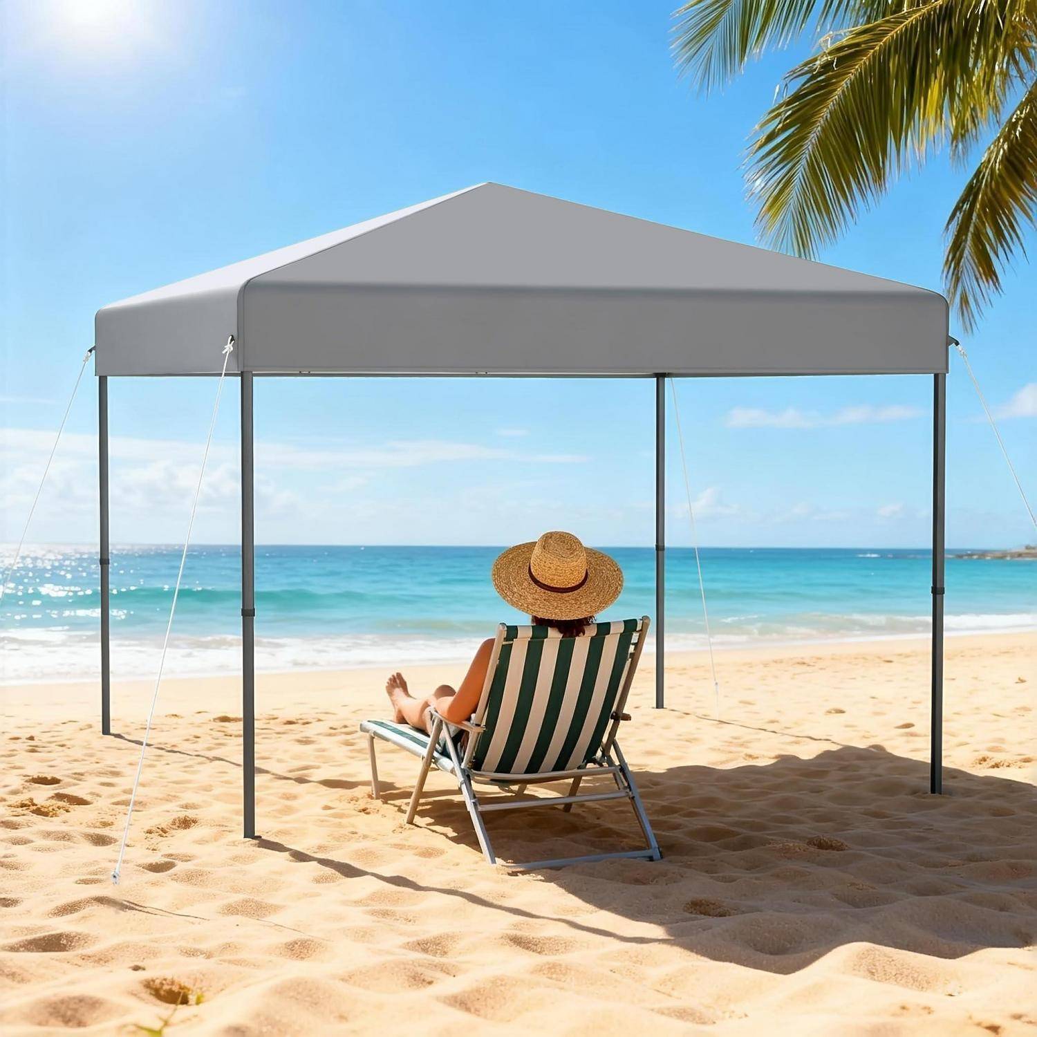 Person, die sich auf einem gestreiften Strandkorb unter einem grauen Sonnenschirm an einem sonnigen tropischen Strand entspannt und zum Ozean blickt.