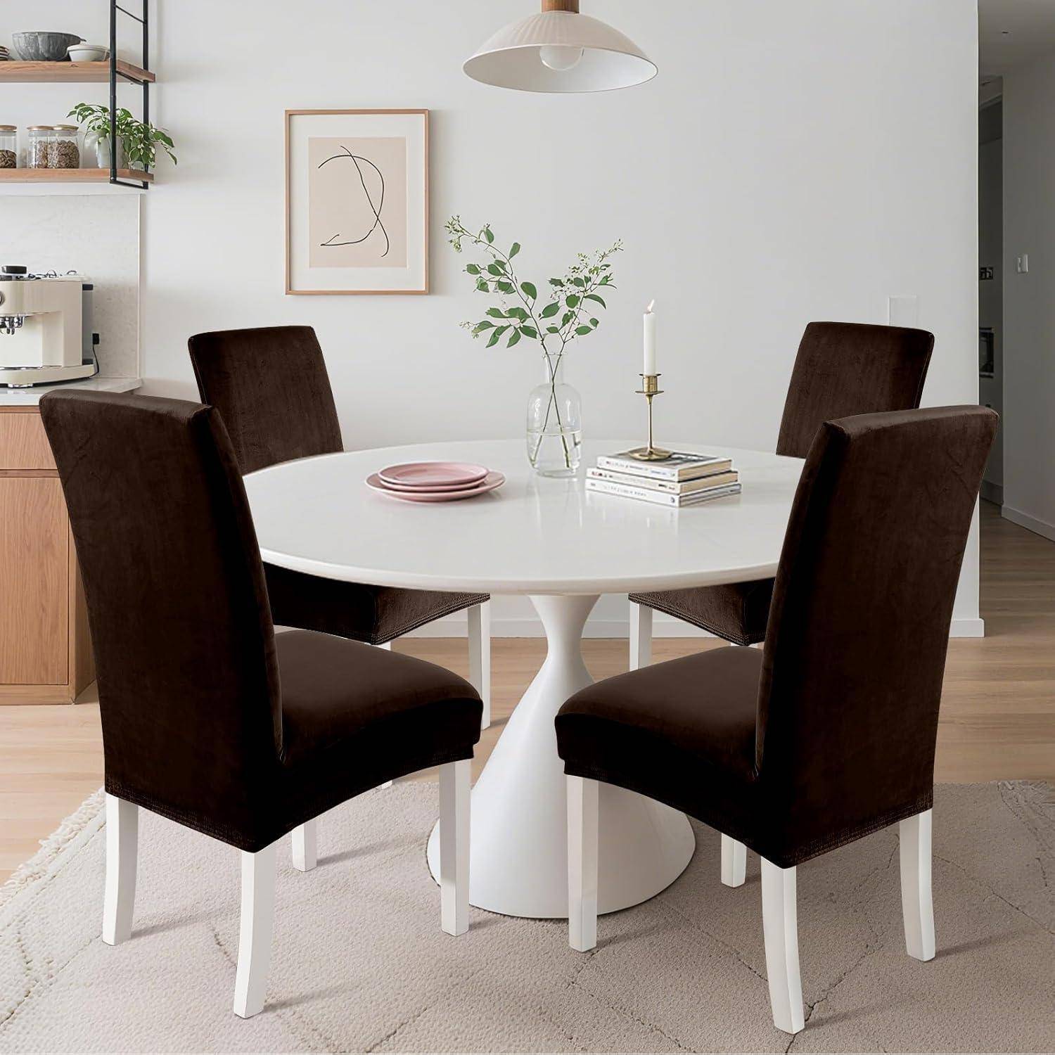 Moderner Essbereich mit weißem rundem Tisch für vier dunkle Stühle gedeckt, rosa Tellern, Büchern, Vase und Kerze in einem minimalistischen Raum.