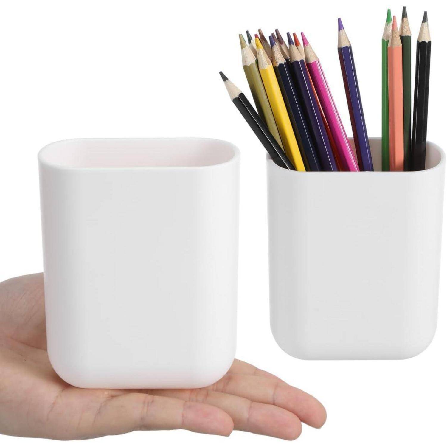 Eine Hand, die eine kleine weiße Tasse neben einer ähnlichen weißen Tasse mit Buntstiften hält, zeigt die Größe des Behälters und seine Verwendung als Stifthalter.