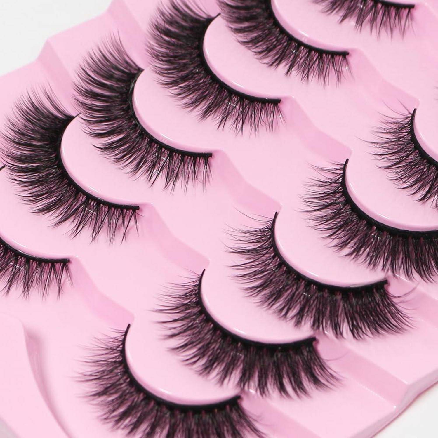 Mehrere Paare von künstlichen Wimpern auf rosa Rückseiten-Karten angeordnet, in einer nahaufnahmeartigen Produktpräsentation gezeigt.