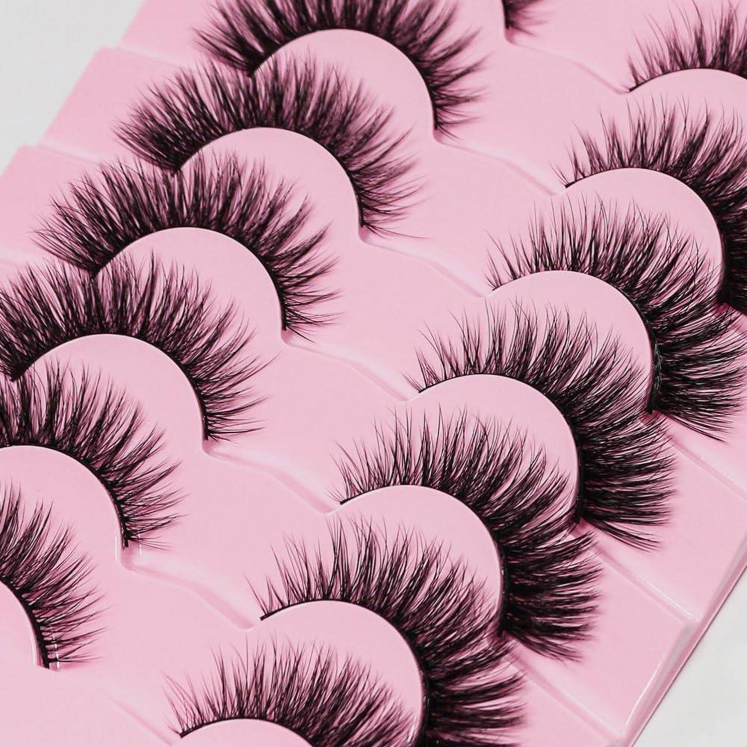 Nahaufnahme von mehreren Paaren langer schwarzer künstlicher Wimpern, die auf rosa Untergrund angeordnet sind, wahrscheinlich eine Schönheitsprodekt-Ausstellung.