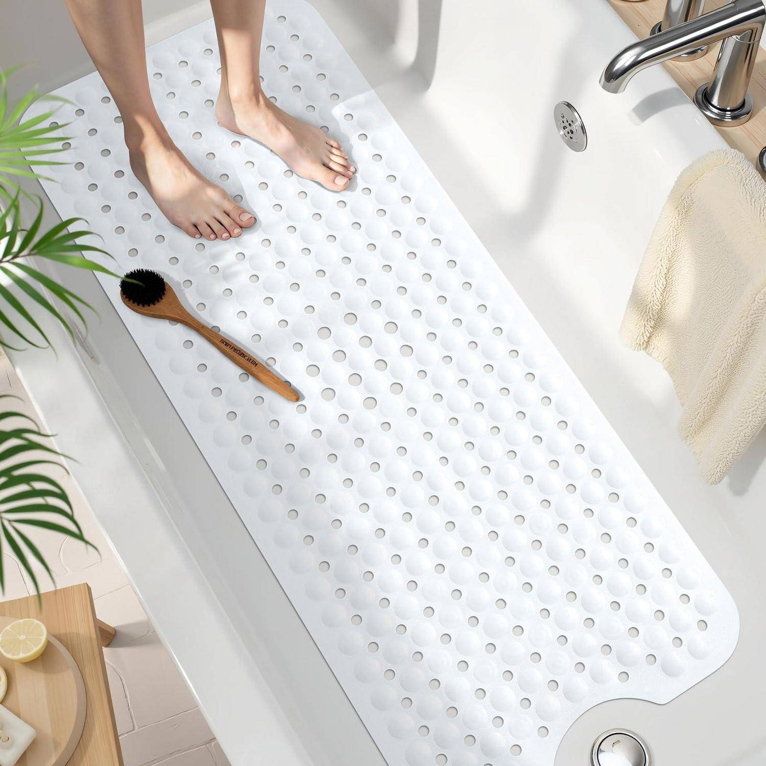 Füße stehen auf einer weißen strukturierten rutschfesten Badewannenmatte in einer Badewanne, mit einer Holzbürste und einem Handtuch in der Nähe.