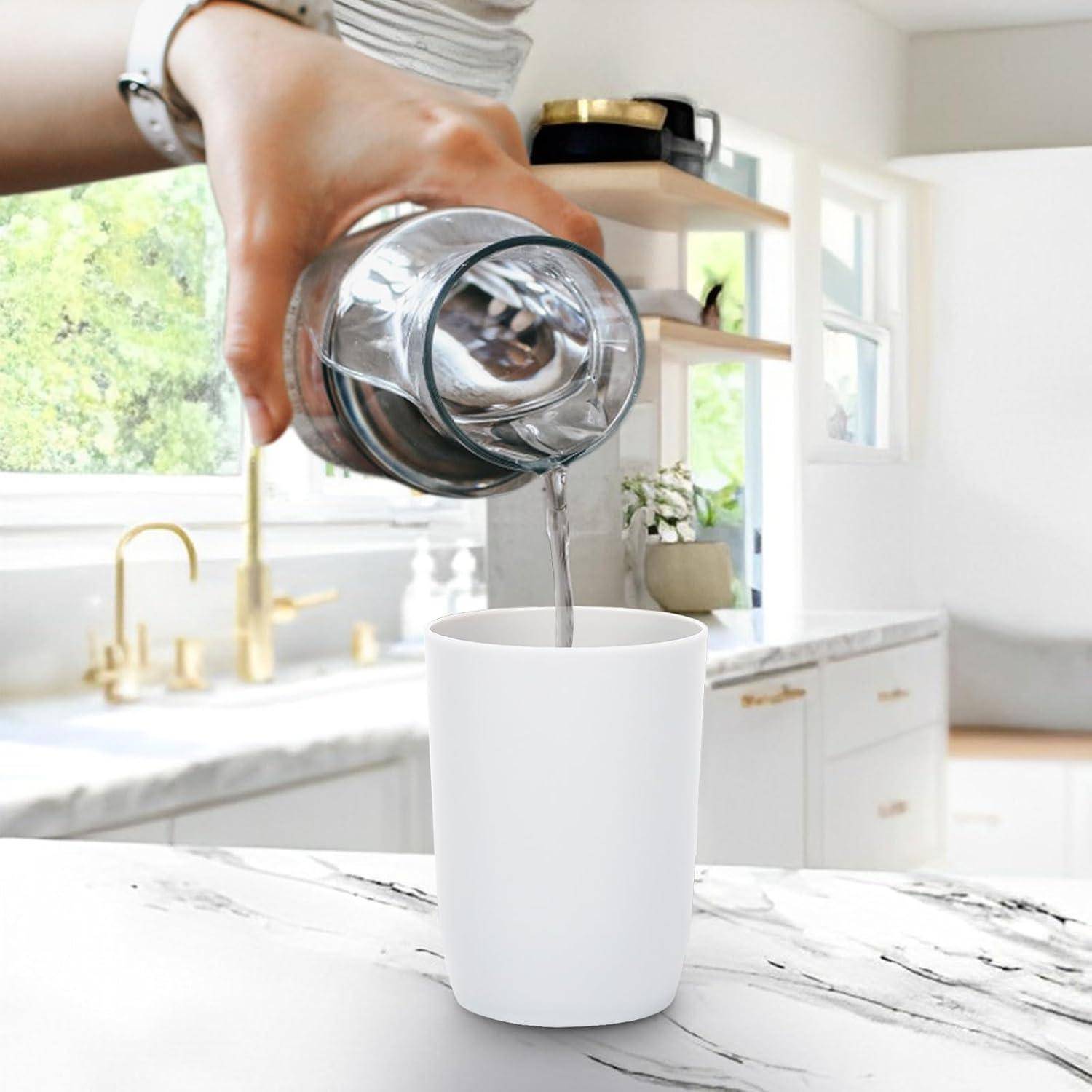 Eine Hand gießt Wasser aus einem Glaskrug in einen weißen Becher in einer hellen Küche.
