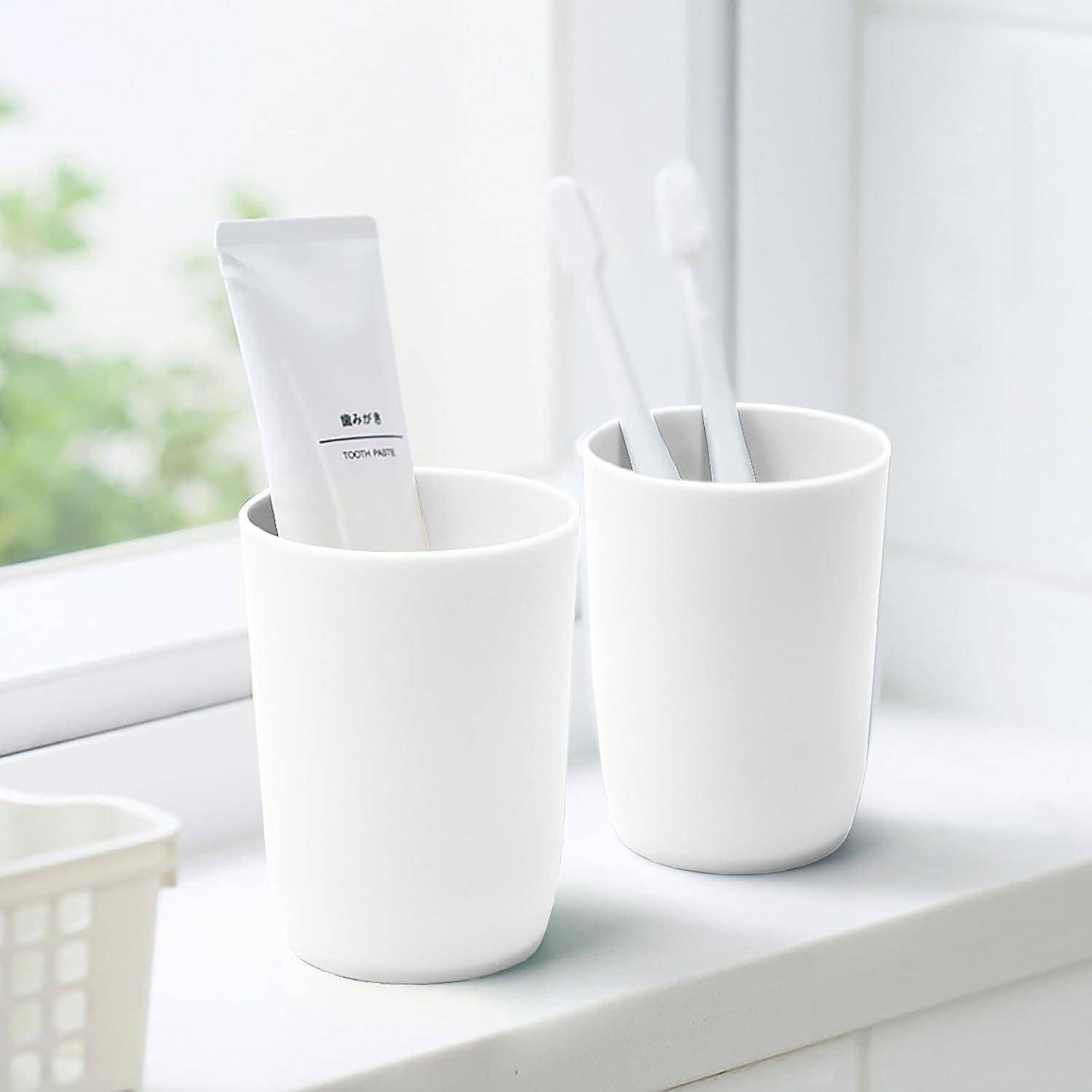 Zwei weiße Tassen auf einer Fensterbank halten Zahnbürsten und eine Zahnpastatube in einem hellen, minimalistischen Badezimmer.