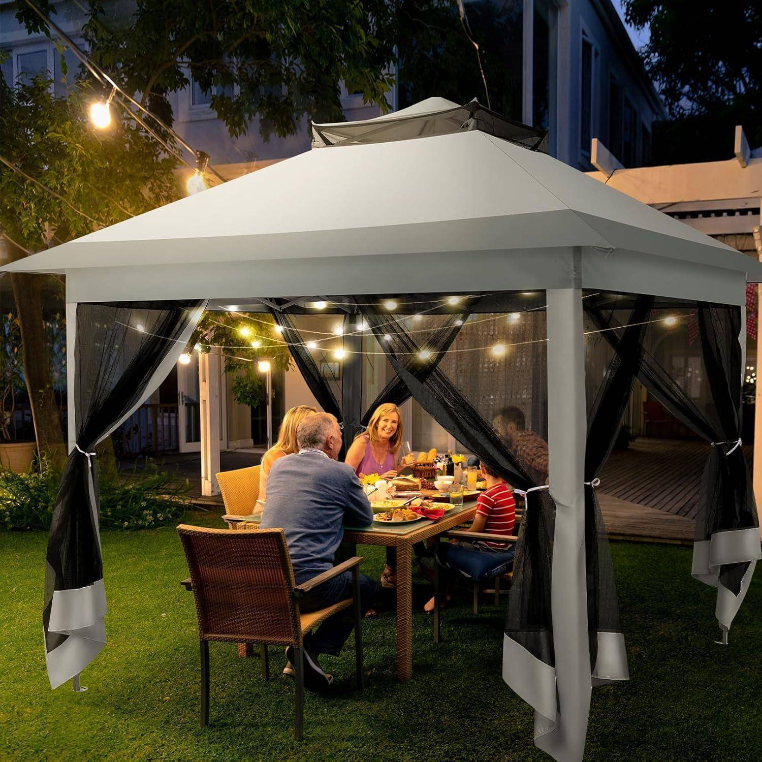 Familie, die nachts unter einer beleuchteten Gartenlaube zusammen isst, sitzt um einen Tisch mit Speisen und Getränken.