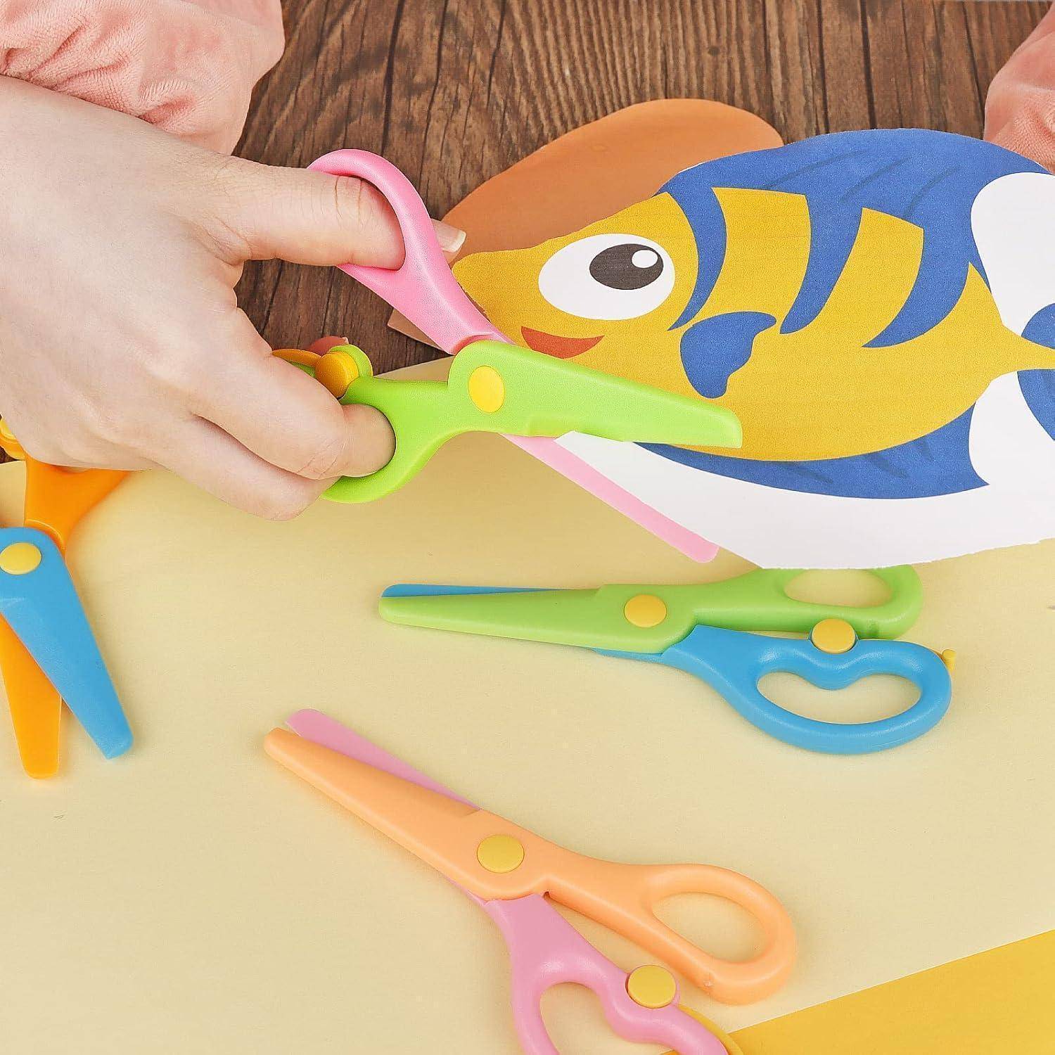 Kind mit Plastikschere, das einen bunten Fisch aus Papier ausschneidet, mit mehreren Scheren, die auf dem Tisch verstreut sind.