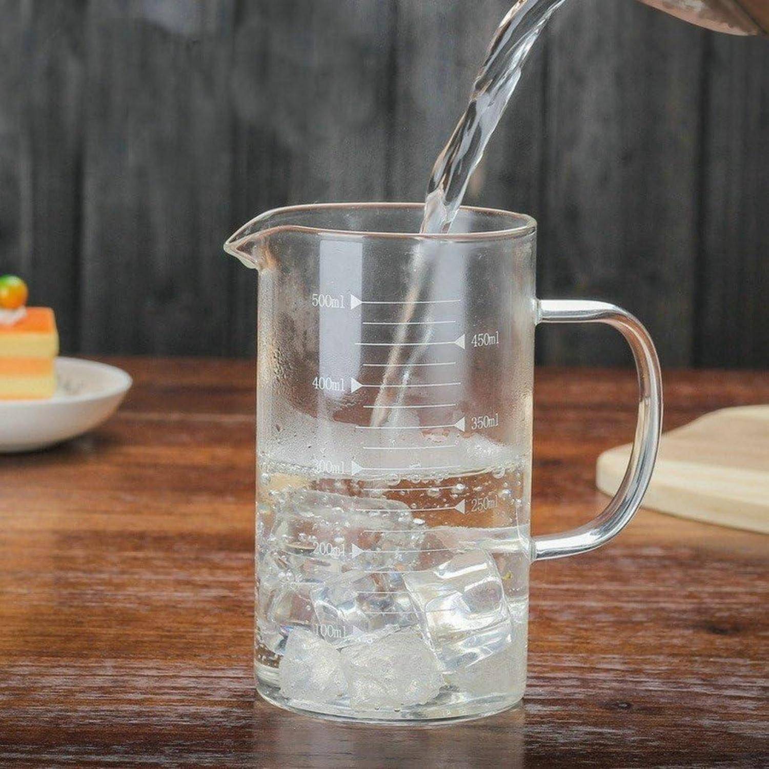 Wasser wird in einen klaren Glaskrug zum Messen gegossen, der mit Eis gefüllt ist, auf einem Holztisch.