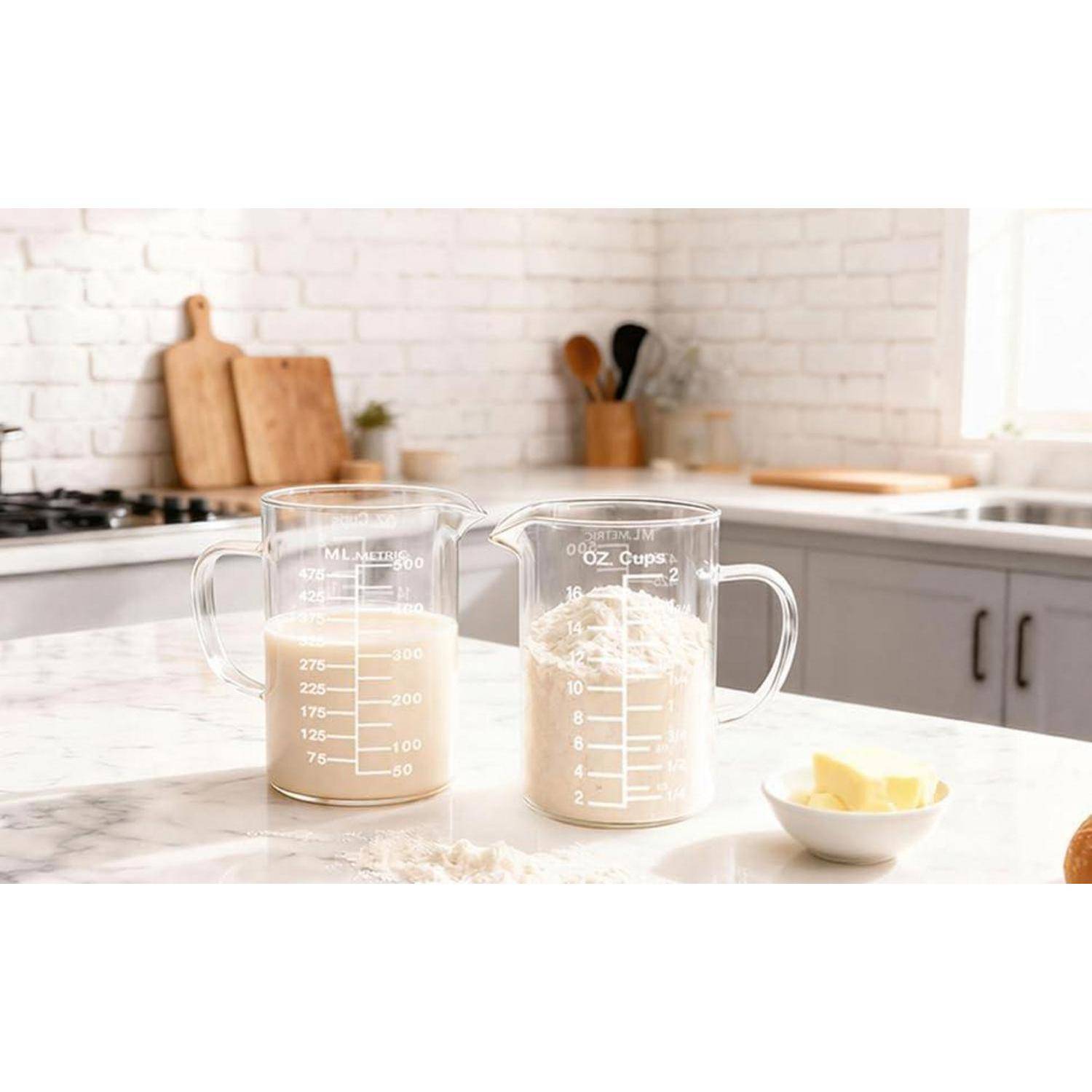 Zwei Glesmessbecher gefüllt mit weißen Zutaten stehen auf einer Küchentheke neben einer kleinen Schüssel mit Butter.
