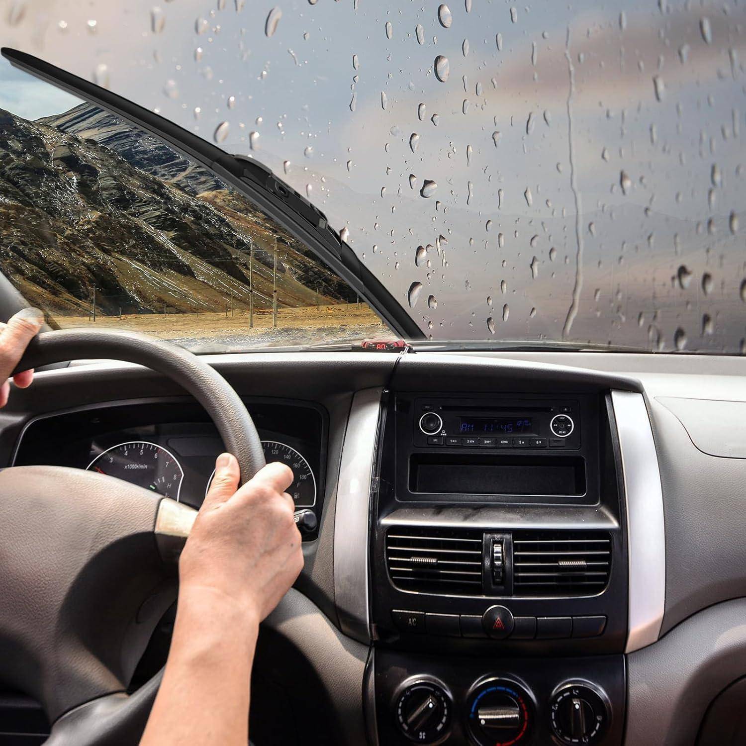 Blick des Fahrers aus dem Inneren eines Autos bei Regen, mit Händen am Lenkrad und Regentropfen auf der Windschutzscheibe.