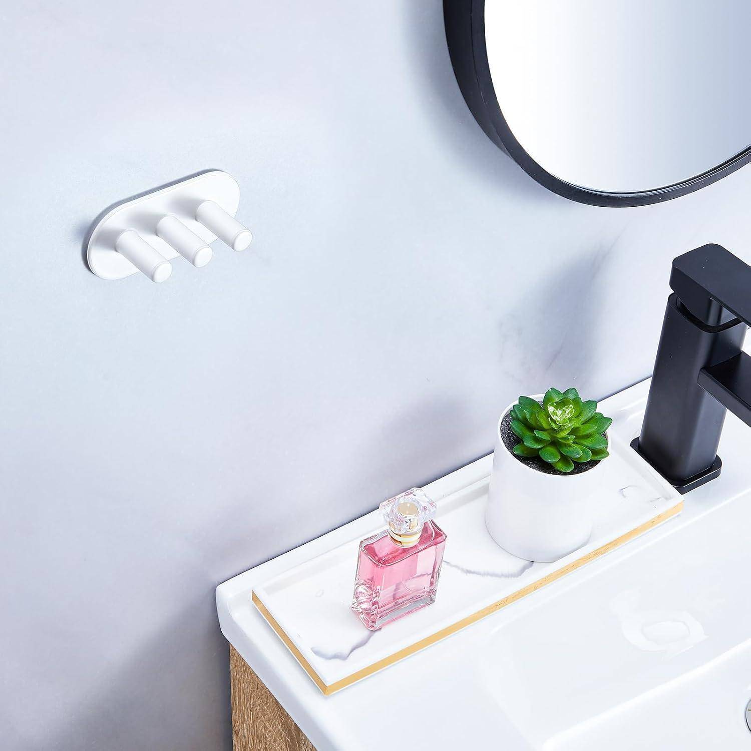 Minimalistische Badezimmerecke mit Waschbecken, wandmontiertem Wasserhahn, rundem Spiegel, Seifenspender, rosa Parfümflasche und kleinem Sukkulenten in einem Topf auf einem Tablett.