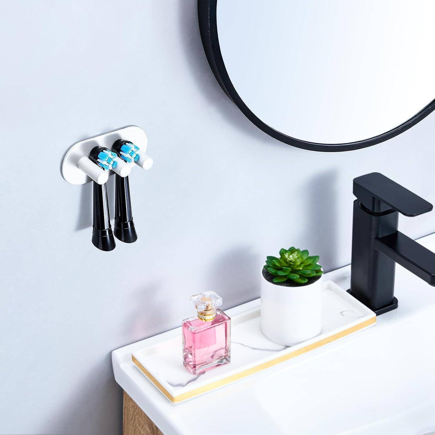 Moderner Waschbereich mit schwarzem Wasserhahn, an der Wand montiertem Zahnbürstenhalter, Seifenschale mit rosa Parfümflasche und kleiner Topfpflanze neben einem runden Spiegel.