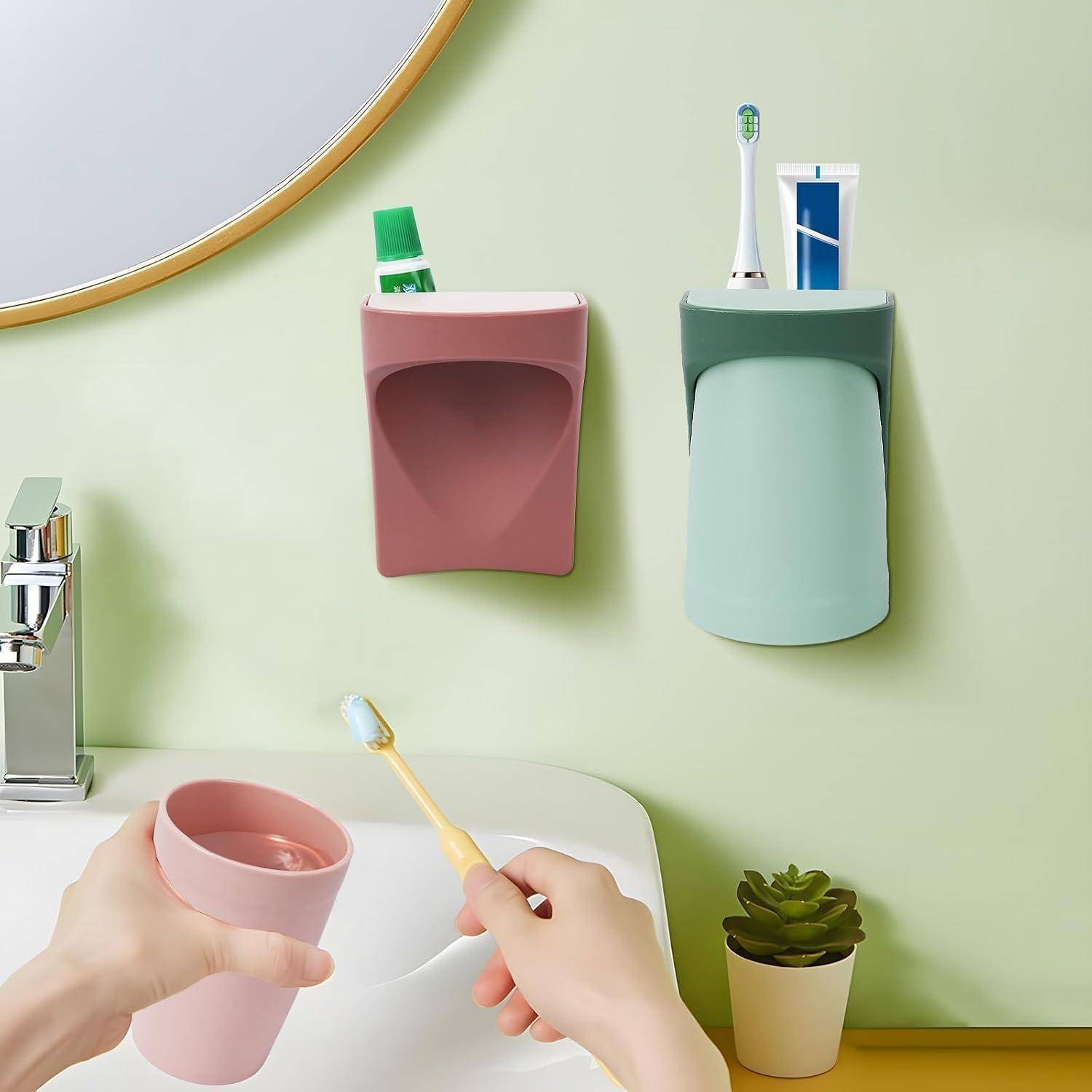 Hände halten eine Tasse und eine Zahnbürste an einem Waschbecken, mit an der Wand montierten Badezimmerhaltern für Zahnpasta und Zahnbürste, einem Spiegel, einem Wasserhahn und einer kleinen Topfpflanze.