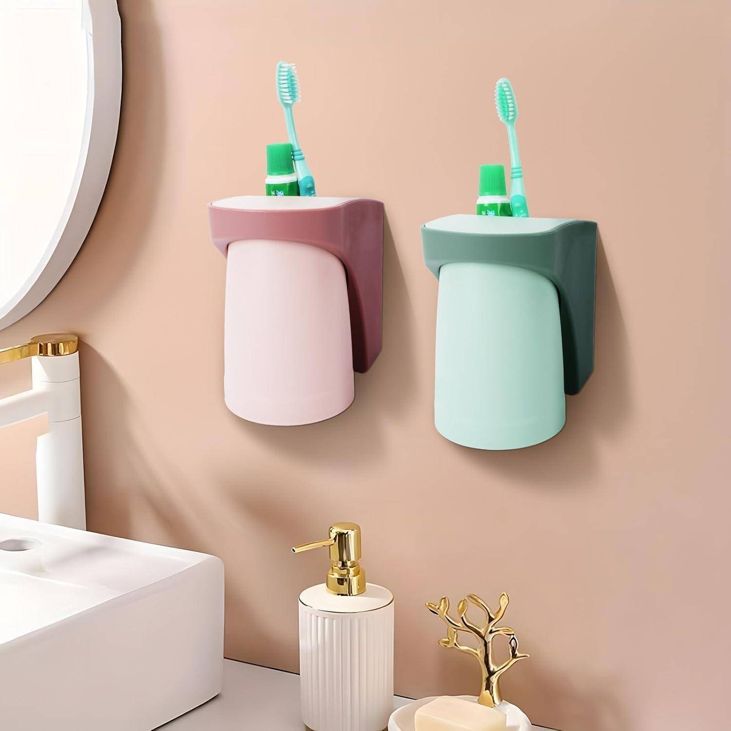 Zwei wandmontierte Zahnbürstenhalter in Rosa und Minzgrün hängen über einem Badezimmerspülbecken, jeder mit einer Zahnbürste und Zahnpasta gefüllt.
