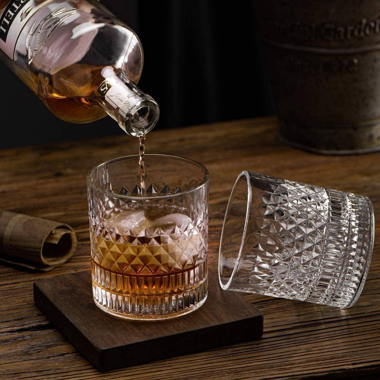 Whiskey wird aus einer Flasche in ein facettiertes Glas auf einem Holzuntersetzer gegossen, während ein weiteres leeres Glas daneben auf einem rustikalen Tisch liegt.