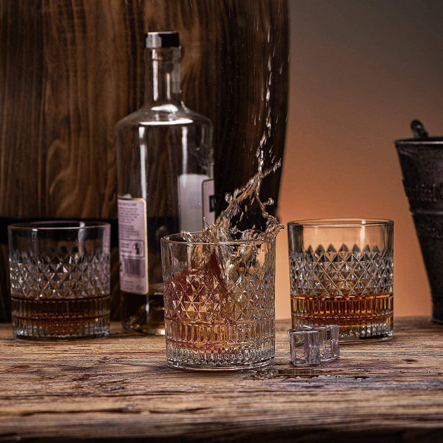 Whiskey wird in ein geschliffenes Glas auf einem Holztisch gegossen, mit einer Flasche, zwei weiteren Gläsern und Eiswürfeln in der Nähe.