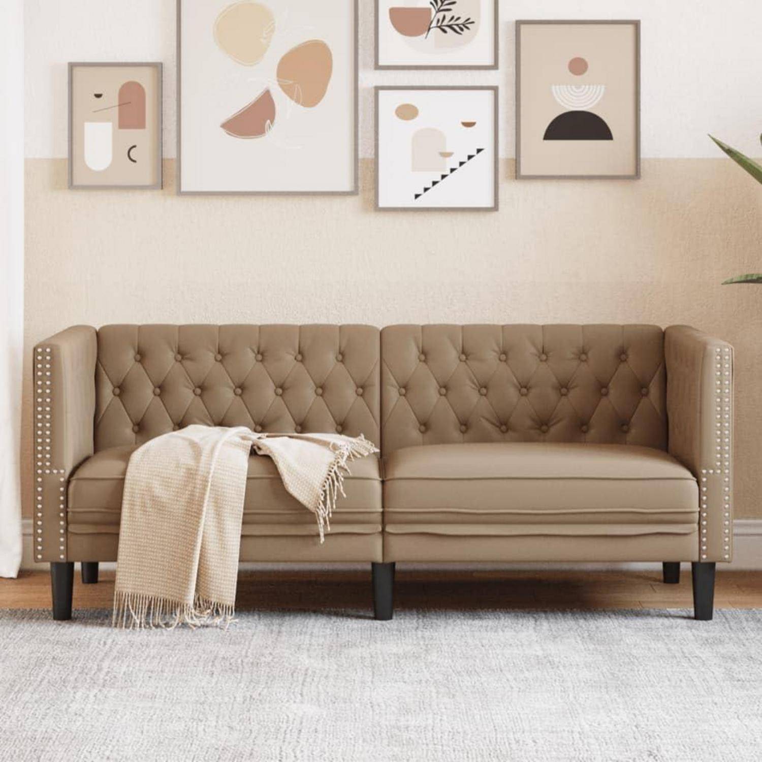 Ein cremefarbenes getufftetes Sofa mit einer cremeweißen Wurfdecke, aufgestellt vor einer Wand mit minimalistischen gerahmten abstrakten Kunstwerken.