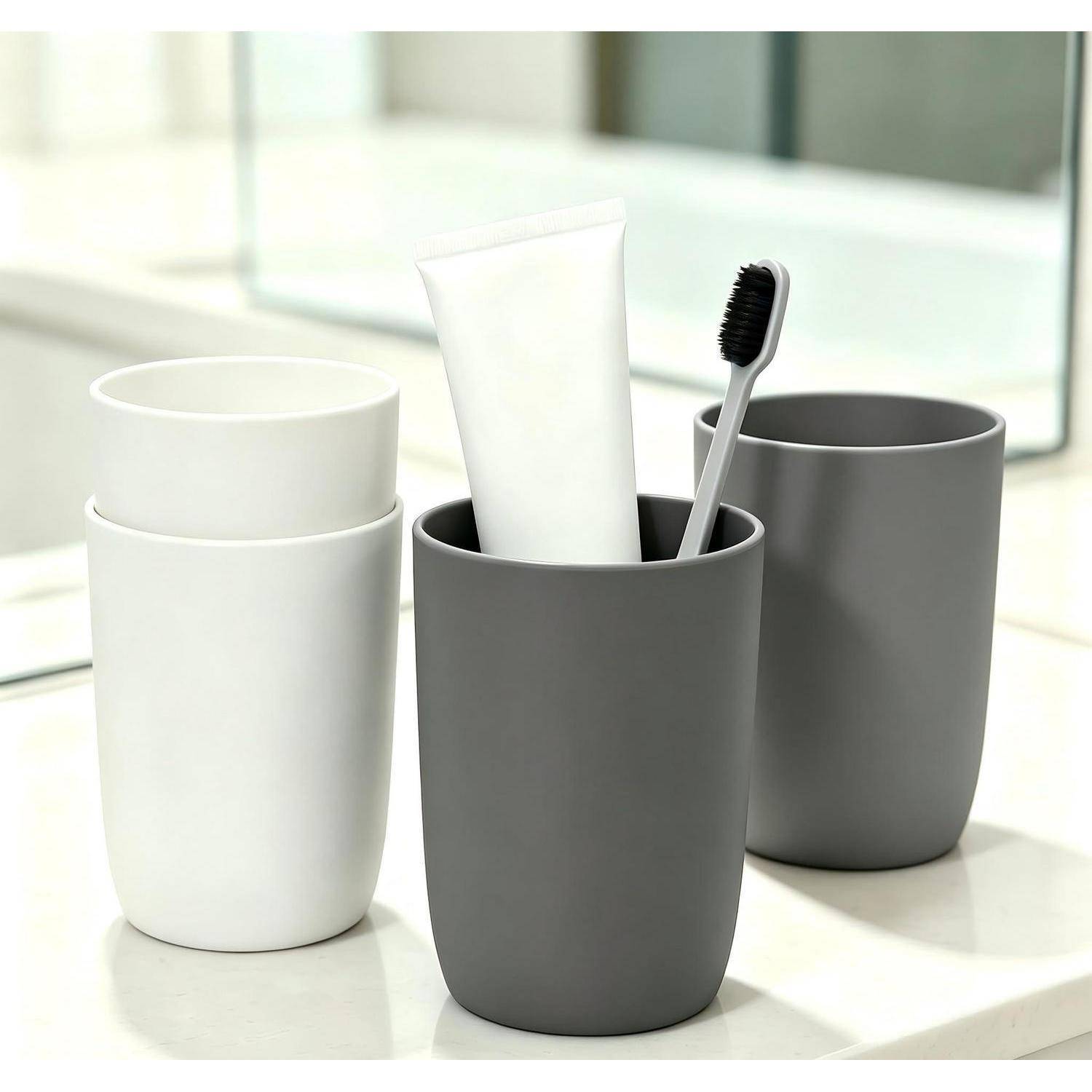 Drei matte Badezimmertassen auf einer weißen Oberfläche, die eine Zahnpastatube und eine Zahnbürste halten, wobei eine Tasse in einer anderen gestapelt ist.