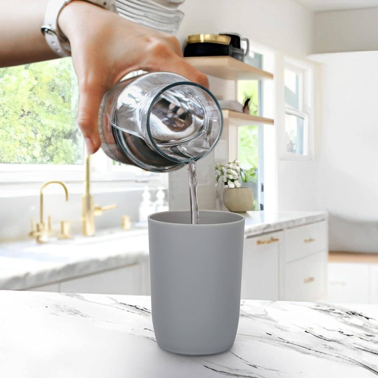Eine Person gießt Wasser aus einer Glasserflasche in eine graue Tasse in einer hellen Küche.