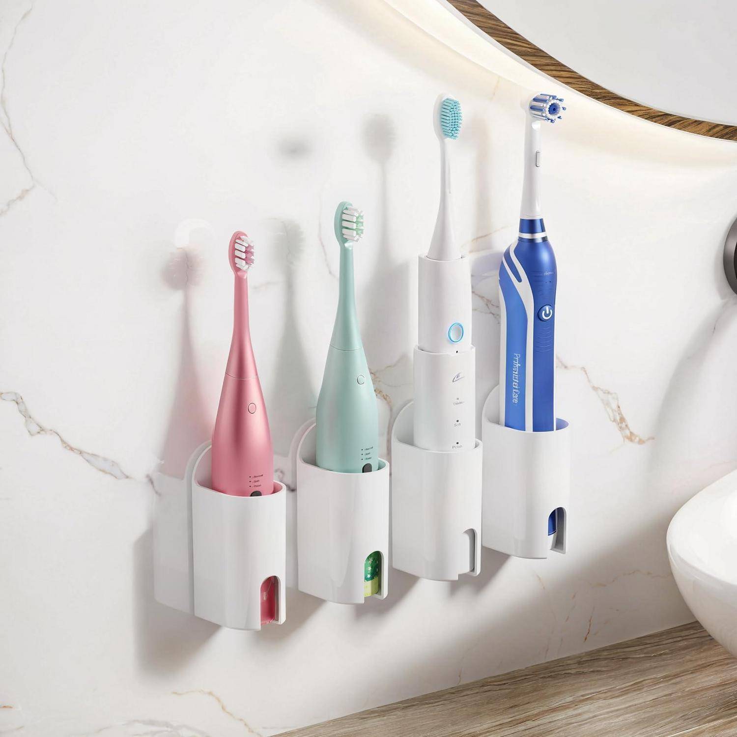 Vier elektrische Zahnbürsten in wandmontierten Haltern neben einem Waschbecken, die einen rosa, mintfarbenen, weißen und blauen Bürstensatz im Badezimmer zeigen.