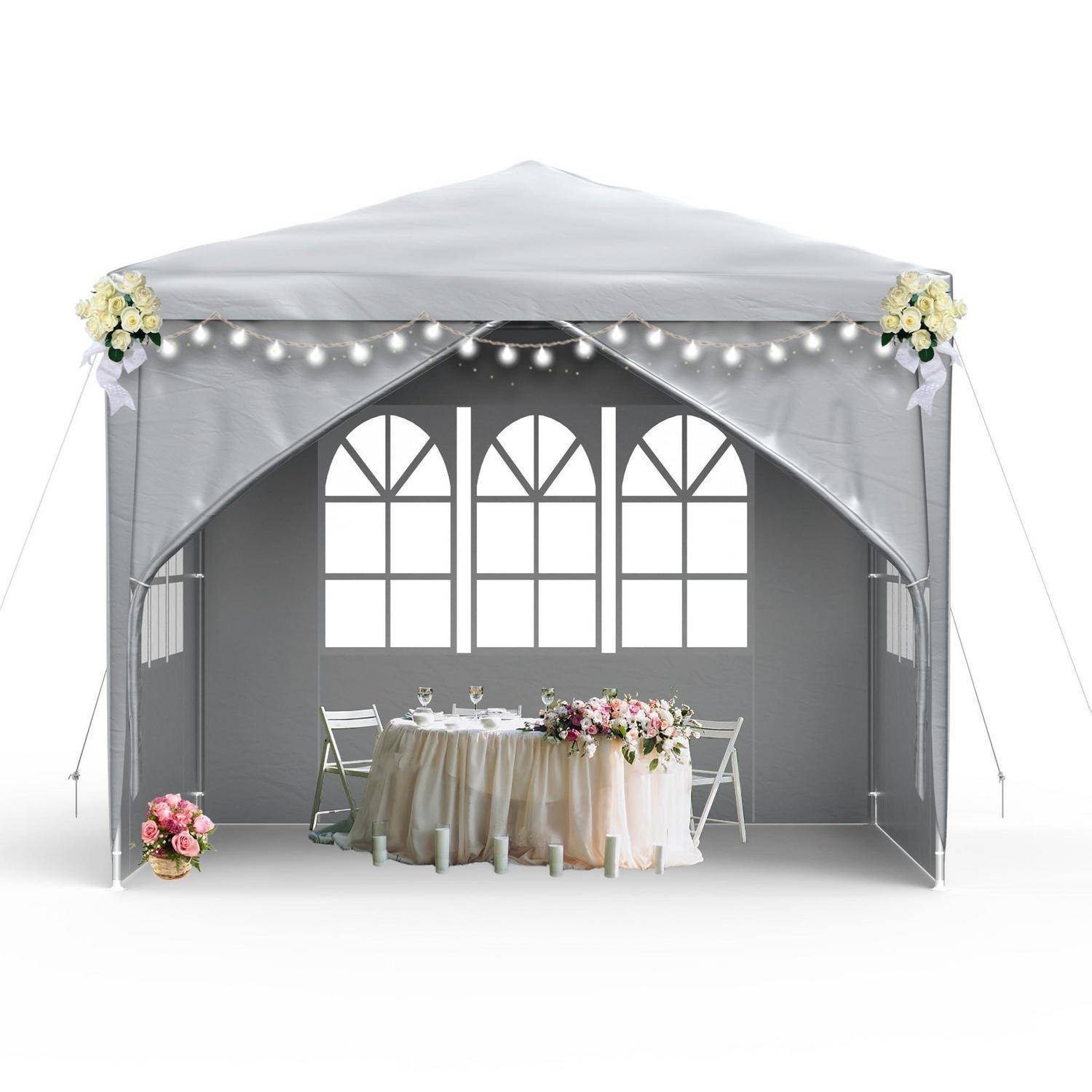 Ein graues Hochzeitszelt mit Lichterketten, Blumendekorationen, ein für zwei Personen eingedeckter Tisch und Stühle in einer dekorierten Veranstaltungsaufstellung.