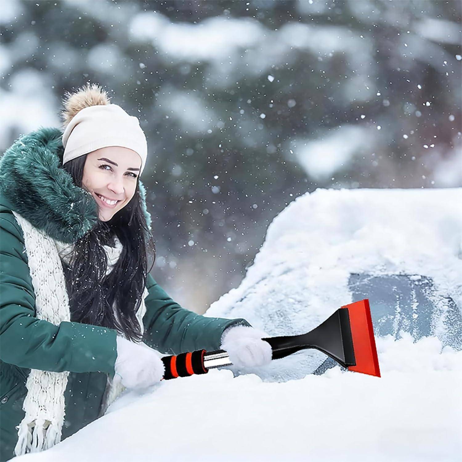 Lächelnde Frau in Winterkleidung kratzt Schnee mit einem Eiskratzer von einer Autowindschutzscheibe ab.