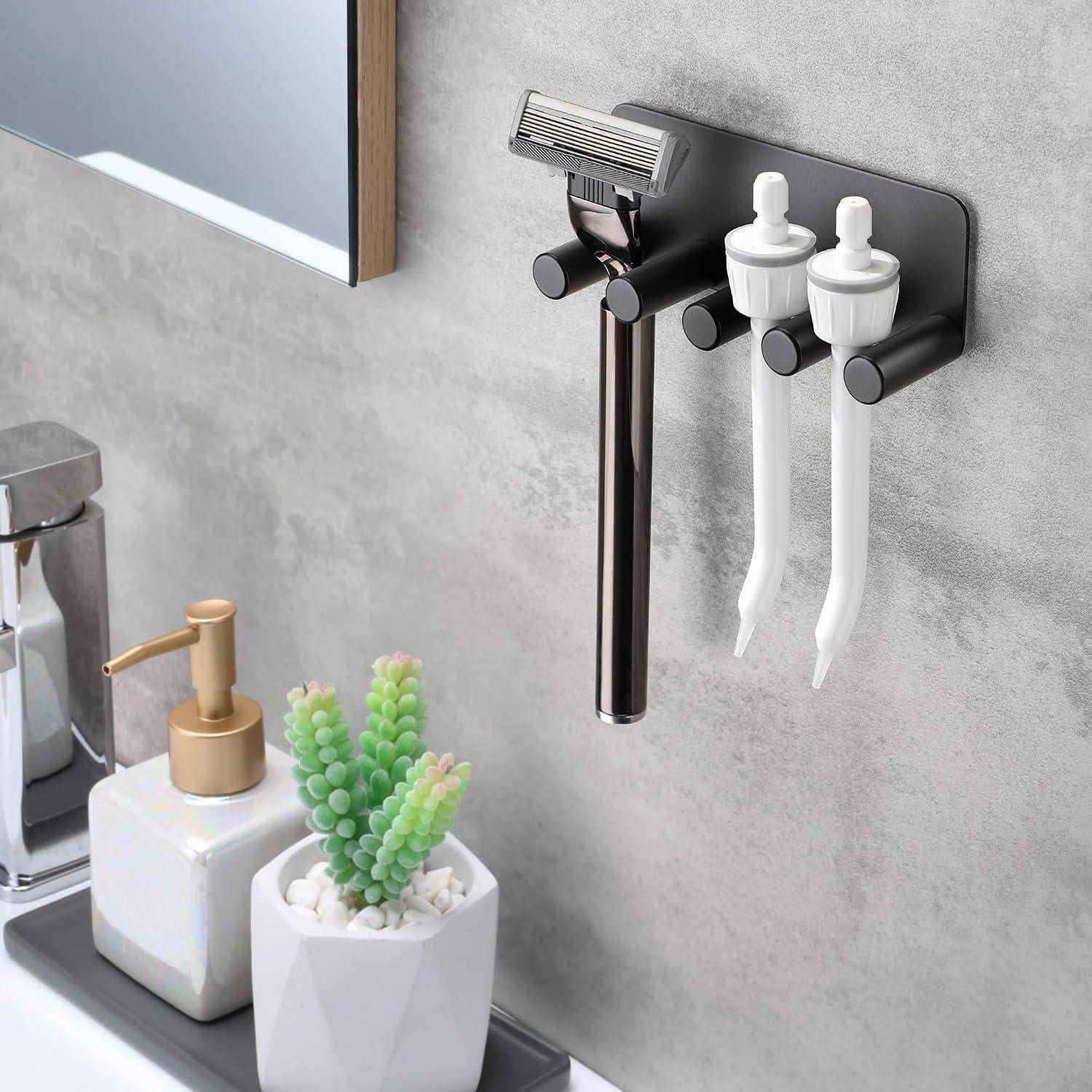 An der Wand montierter Badezimmerorganizer mit Rasiererhalter und zwei Zahnbürstenköpfen über einem Waschbecken, neben einem Seifenspender und kleiner Pflanzendekoration.