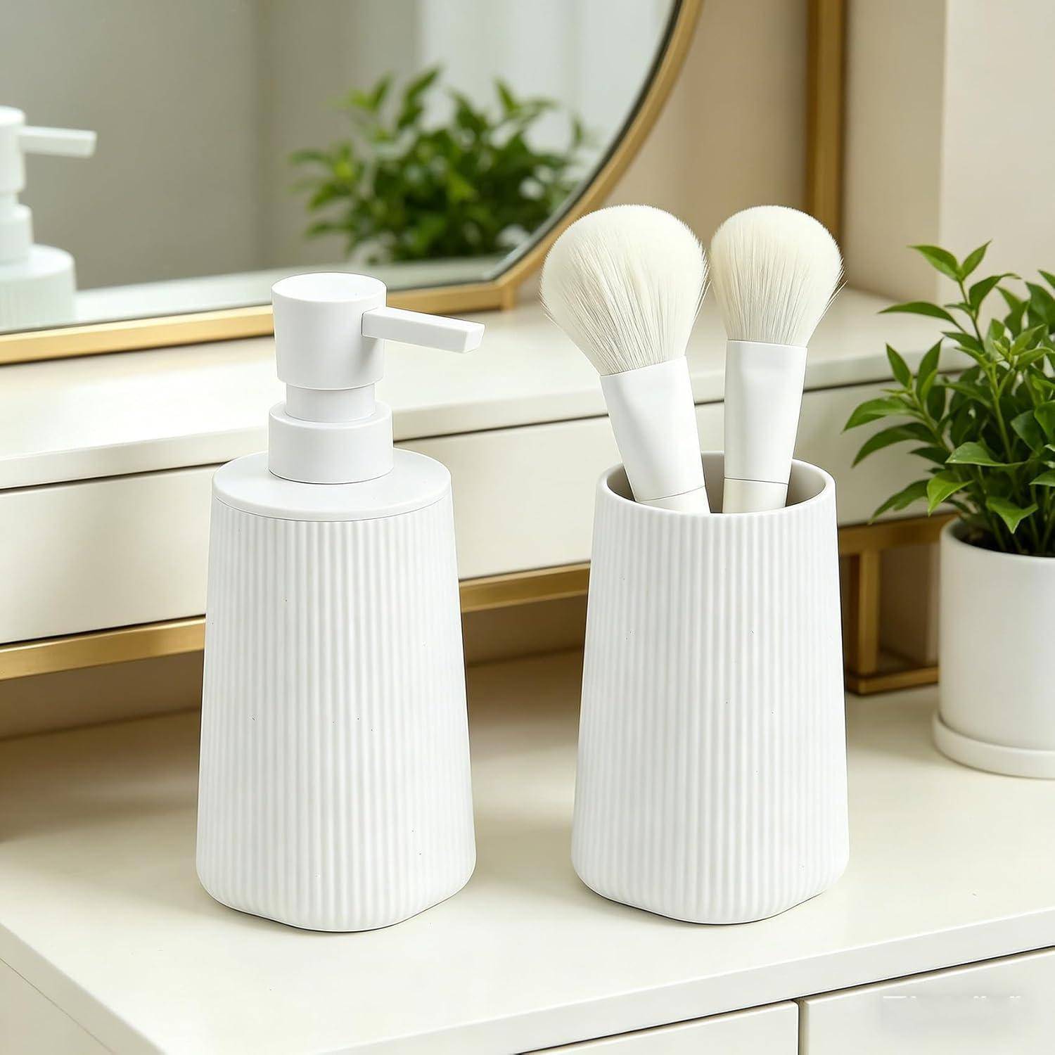 Weißer gerillter Seifenspender und passender Bürstenhalter mit zwei Make-up-Pinseln auf einem Badezimmerwaschbecken neben einem Spiegel und einer Pflanze.