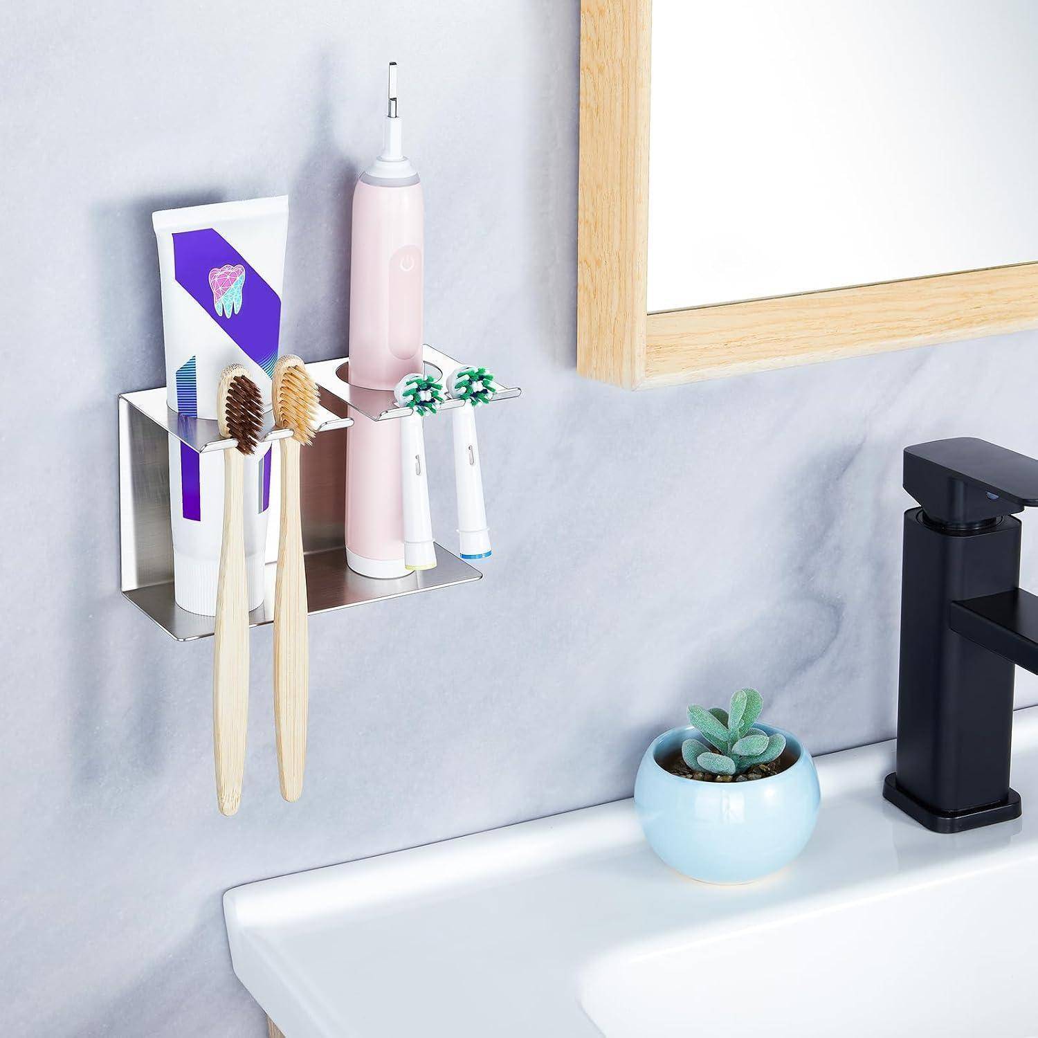 An der Wand montierter Badezimmer-Organizer mit zwei Zahnbürsten, einer Zahnpastatube und einer elektrischen Zahnbürste neben einem Waschbecken und einem Wasserhahn, mit einer kleinen Topfpflanze.
