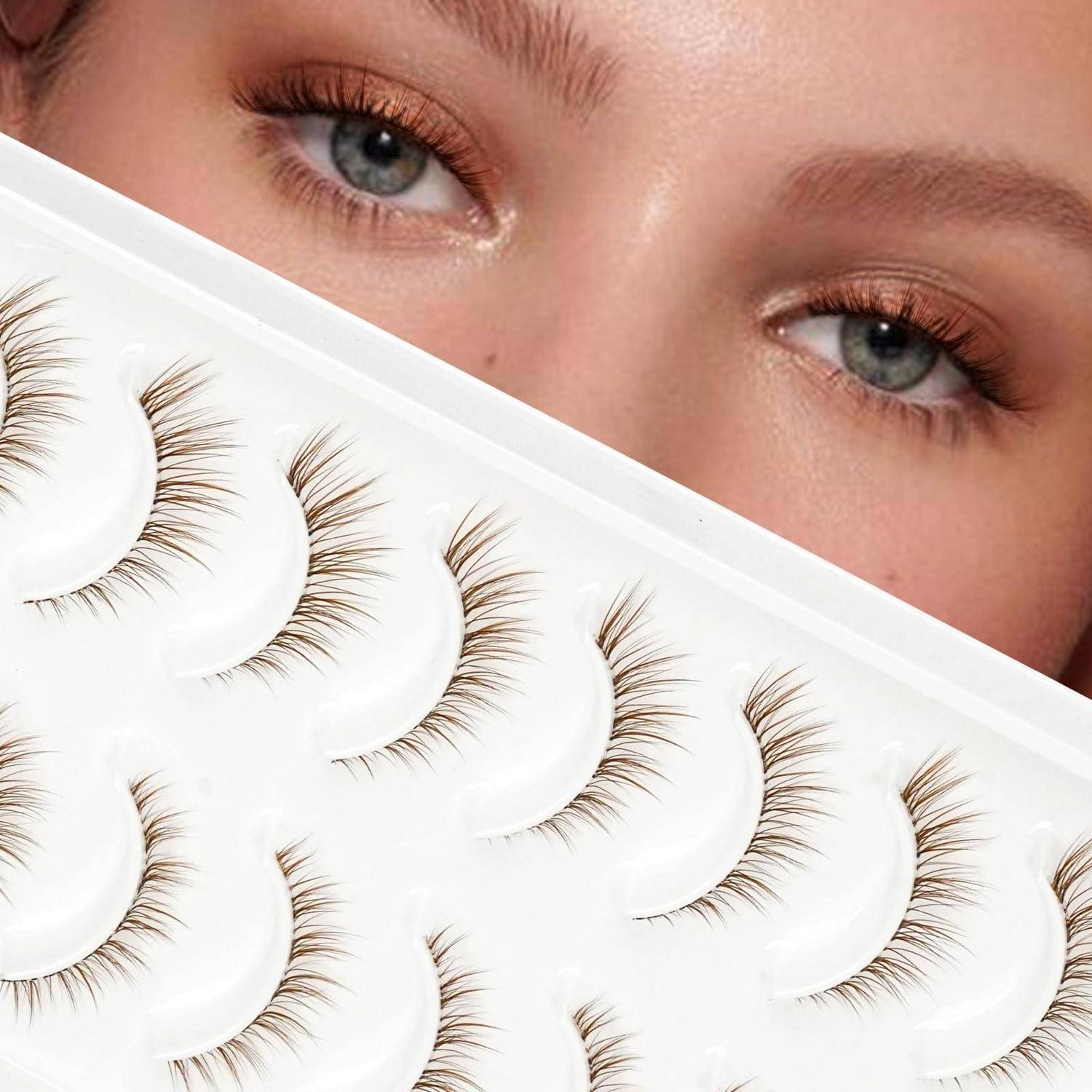 Nahaufnahme von blauen Augen hinter einer Auswahl von falschen Wimpernstreifen auf einem weißen Tablett, was auf ein Beauty- oder Kosmetikproduktbild hindeutet.