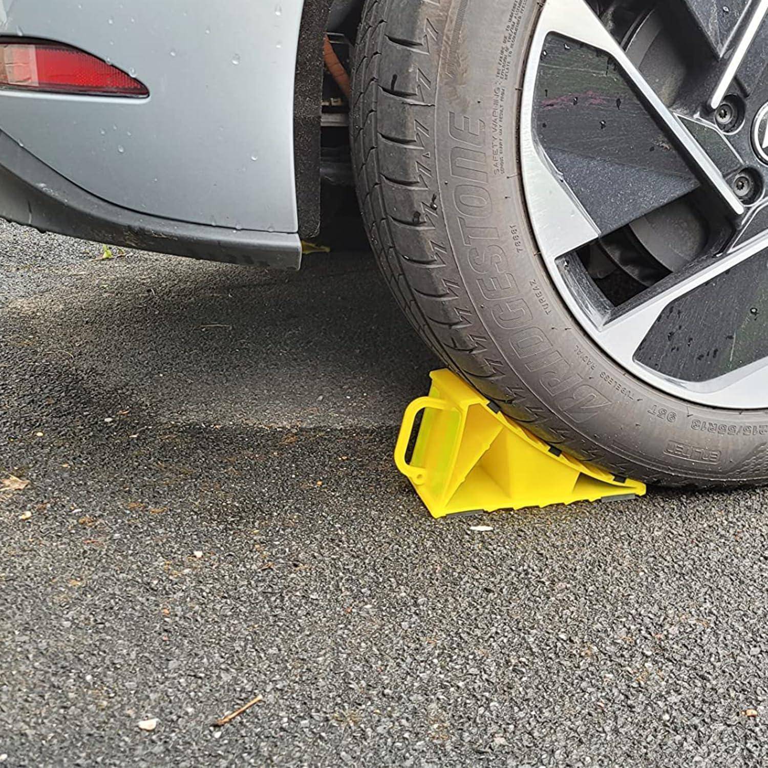 Ein Autoreifen geparkt auf einer leuchtend gelben Radkralle oder einem Parkplatzstiefel auf nassem Pflaster neben einem grauen Fahrzeug.