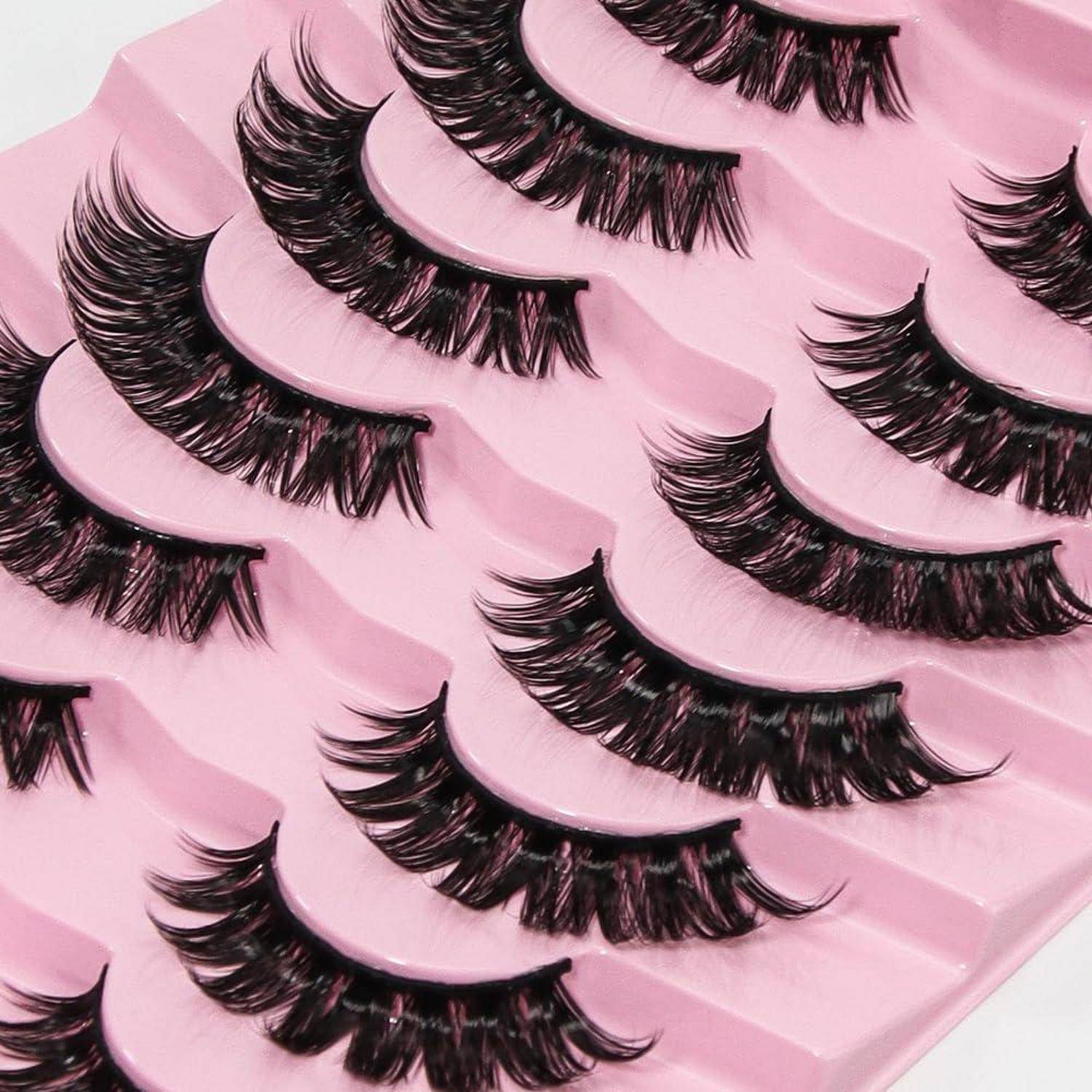 Mehrere Paar künstliche Wimpern in Reihen auf rosa Verpackung angeordnet.
