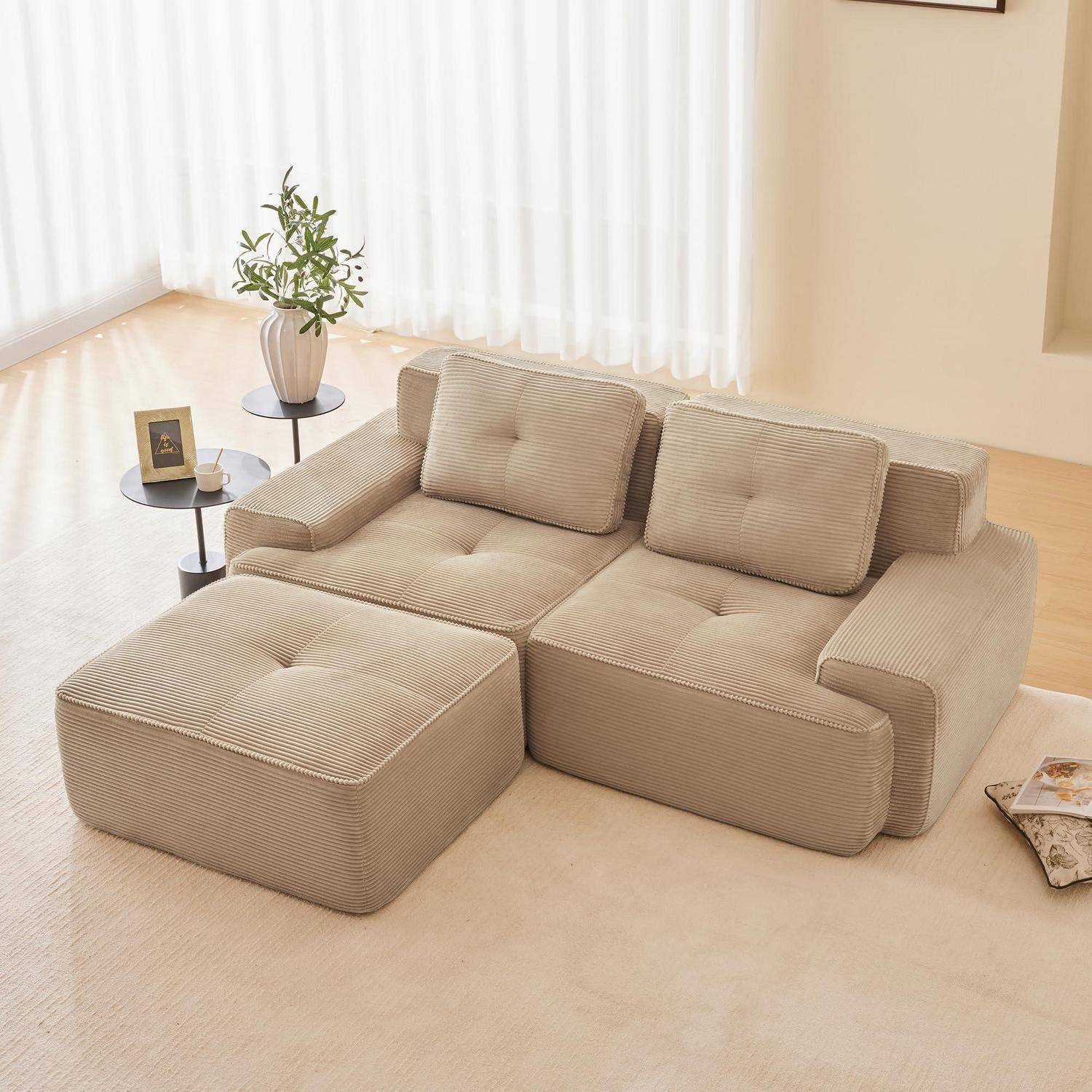 Beiges Cord-Modulsofa mit Ottomane und Kissen in einem hellen Wohnzimmer neben einem kleinen Beistelltisch und einer Pflanze.