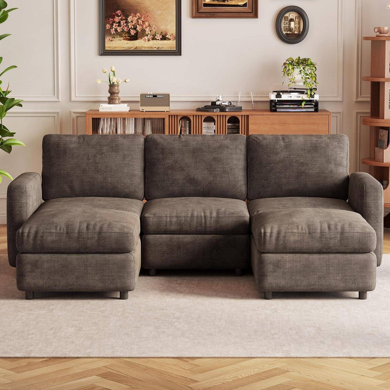 Graues dreierteiliges Ecksofa mit einer mittleren Konsole in einem Wohnzimmer, gezeigt gegen eine Wand mit gerahmten Kunstwerken und einem Holzkommode.