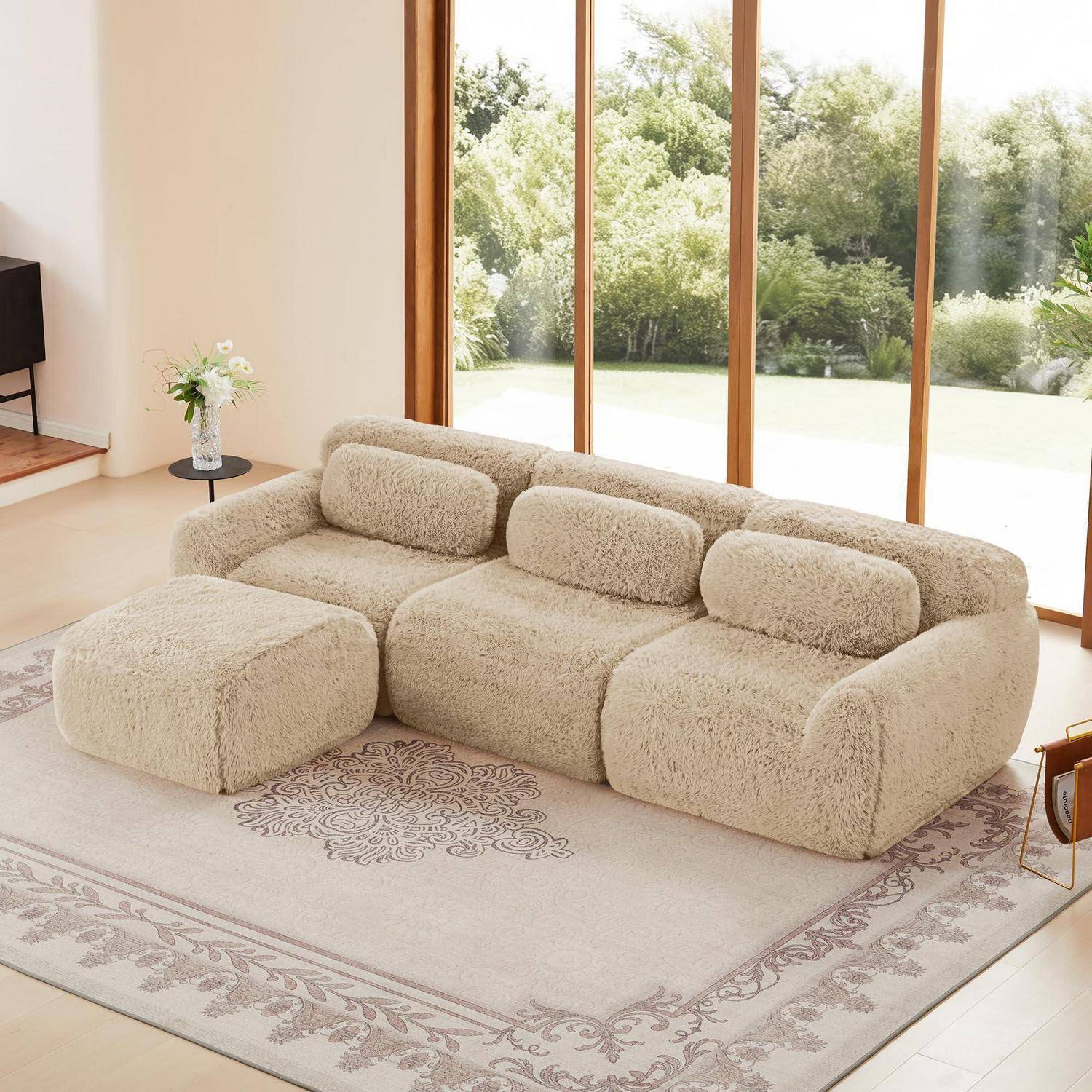 Beigefarbiges Ecksofa mit Ottomane in einem hellen Wohnzimmer vor großen zum Garten gerichteten Fenstern.