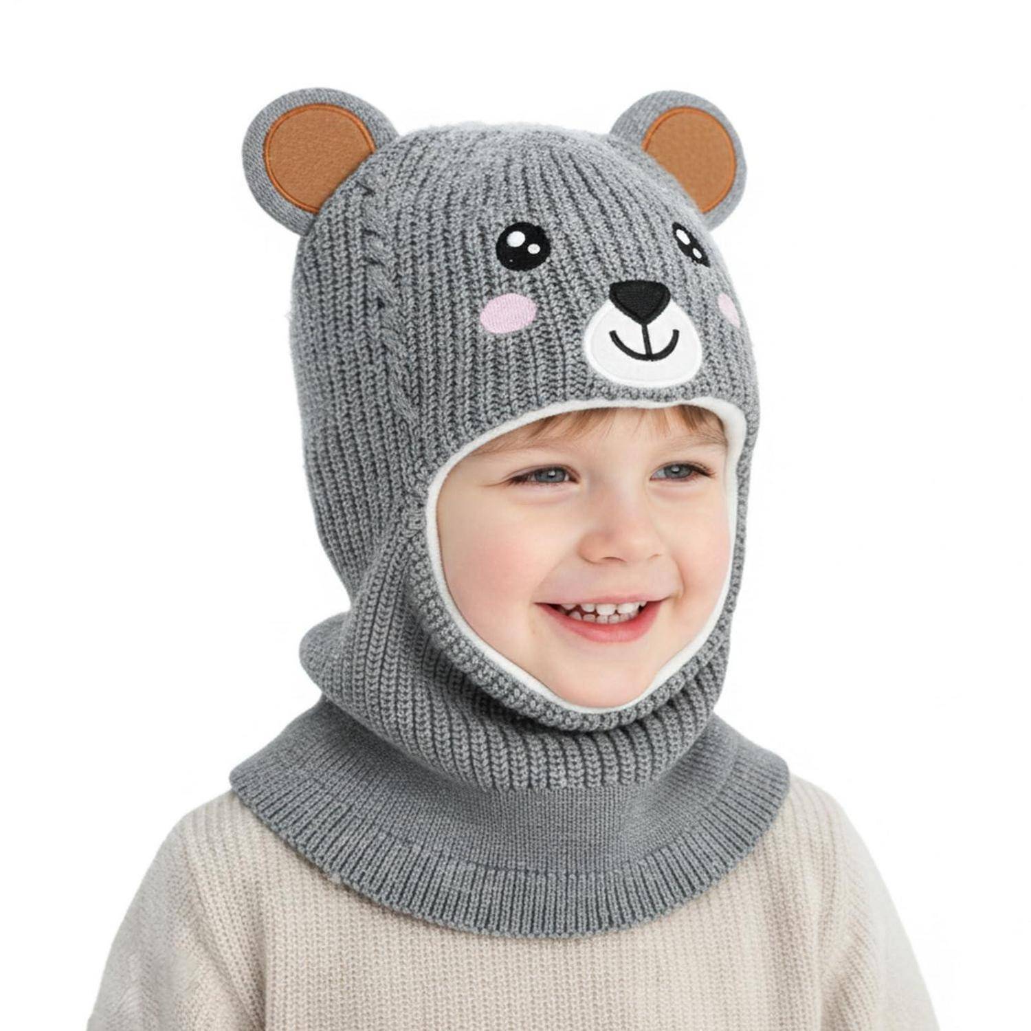 Lachendes Kind, das eine graue gestrickte Bärenmütze mit Ohren und Gesichtsdesign trägt, auf weißem Hintergrund.