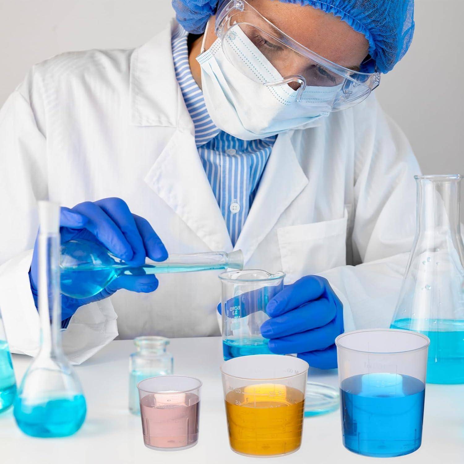 Wissenschaftler im Laborkittel, Maske, Schutzbrille und Handschuhen gießt blaue Flüssigkeit in ein Becherglas zwischen farbigen chemischen Bechergläsern und Flaschen.