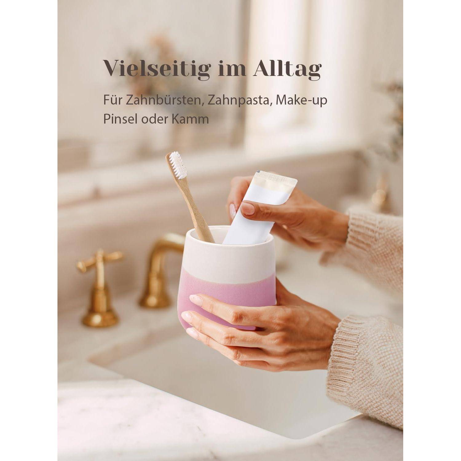 Hände, die einen rosa-weißen Badezimmertasse mit einer Zahnbürste und einer Zahnpastatube halten; deutscher Text besagt, dass sie vielseitig für den täglichen Gebrauch für Zahnbürsten, Zahnpasta, Make-up-Pinsel oder Kämme einsetzbar ist.