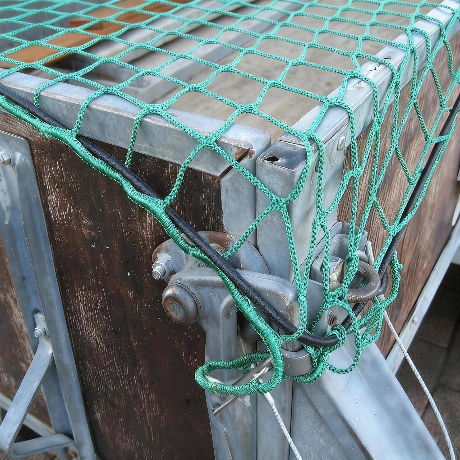 Nahaufnahme eines metallenen Frachtbehälters oder einer Transportkiste, die mit einem grünen Seilnetz über einem Holz- und Stahlrahmen gesichert ist.