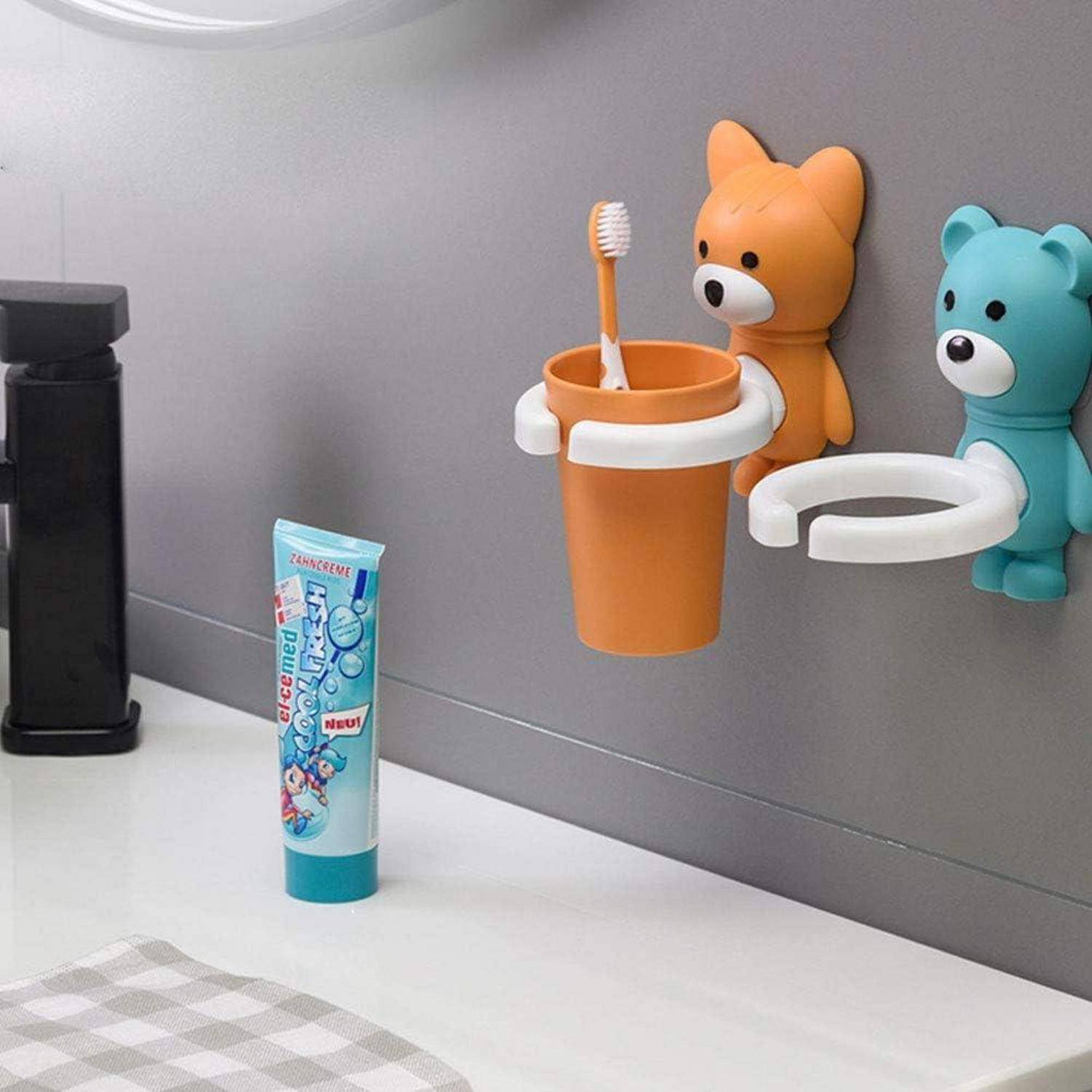 Badezimmerwaschbereich mit zwei Cartoon-Bärhaltern an der Wand, einer hält eine Zahnbürste in einem orangefarbenen Becher und eine Zahnpastatube steht auf der Theke.