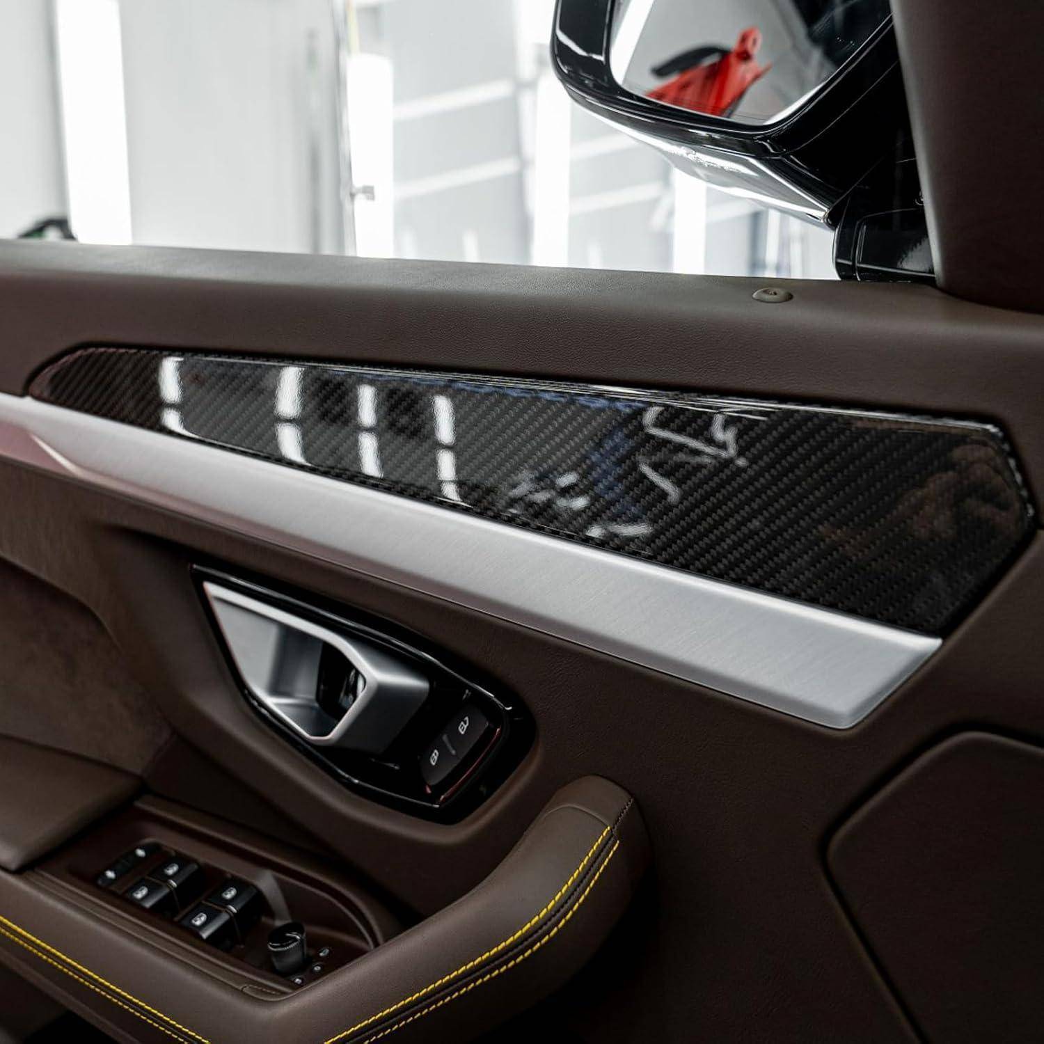 Nahaufnahme eines Luxusautotürinnenraums mit braunem Leder, gelbem Nahtfaden, Kohlefaser-Verkleidung und Fenster- sowie Sitzverstellungen.