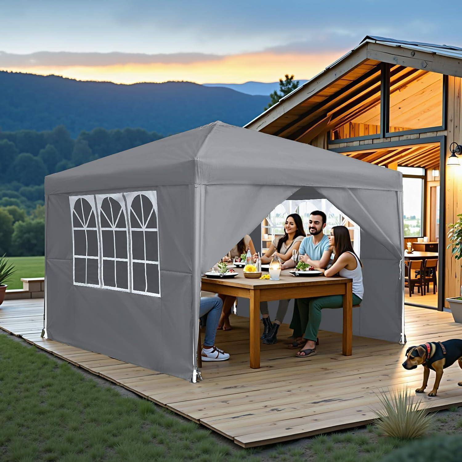Grauer Außen-Gazebo-Zelt auf einer Holzterrasse, mit Menschen, die an einem Tisch neben einem modernen Haus bei Sonnenuntergang speisen.