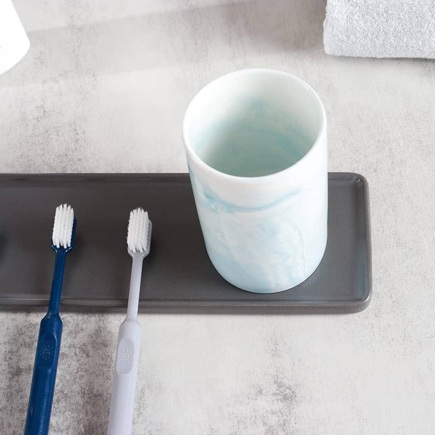 Zwei Zahnbürsten und ein Becher stehen auf einem dunklen Badezimmertablett neben einem Waschbecken.