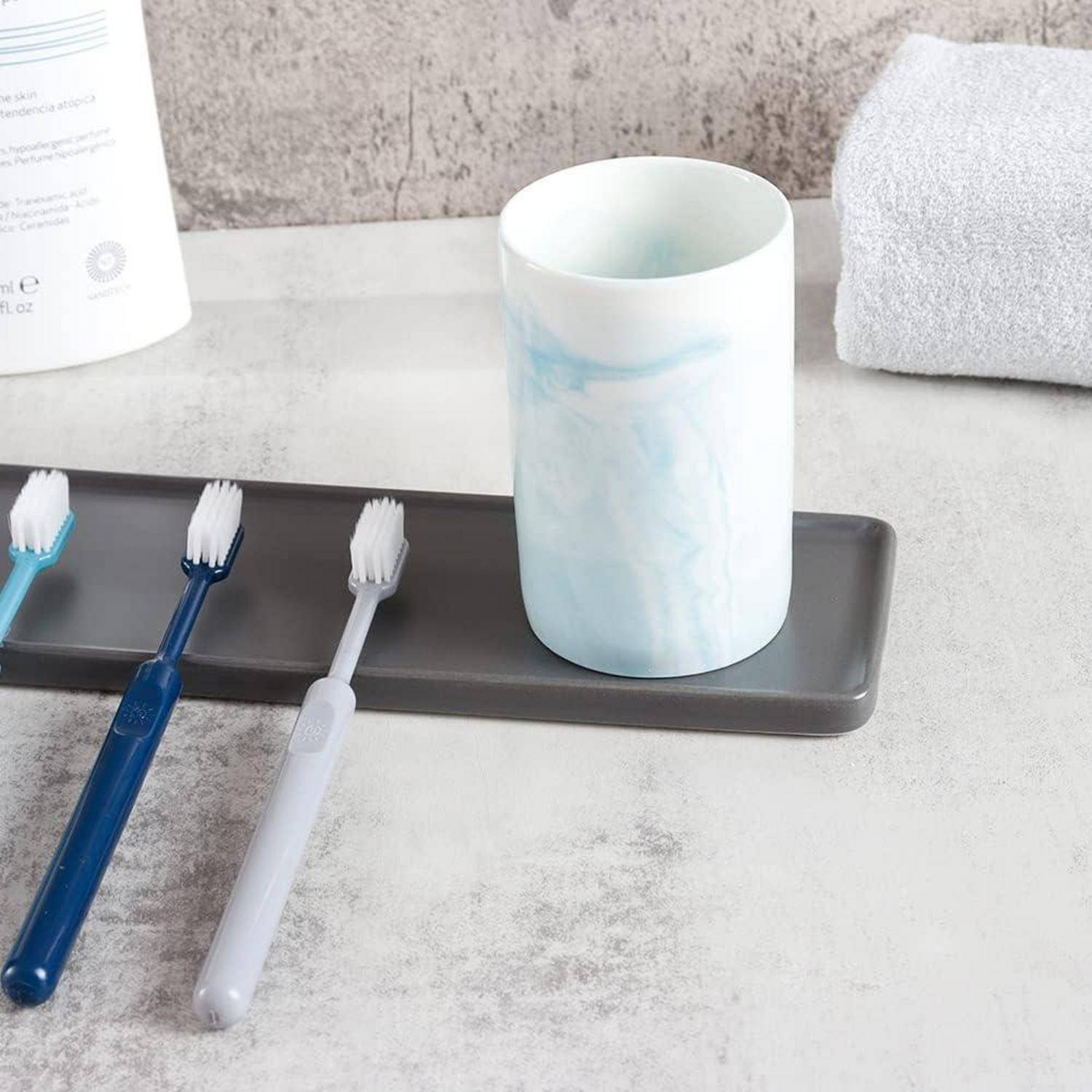 Drei Zahnbürsten und eine weiße Tasse stehen auf einem schwarzen Tablett auf einer Badezimmerablagefläche.