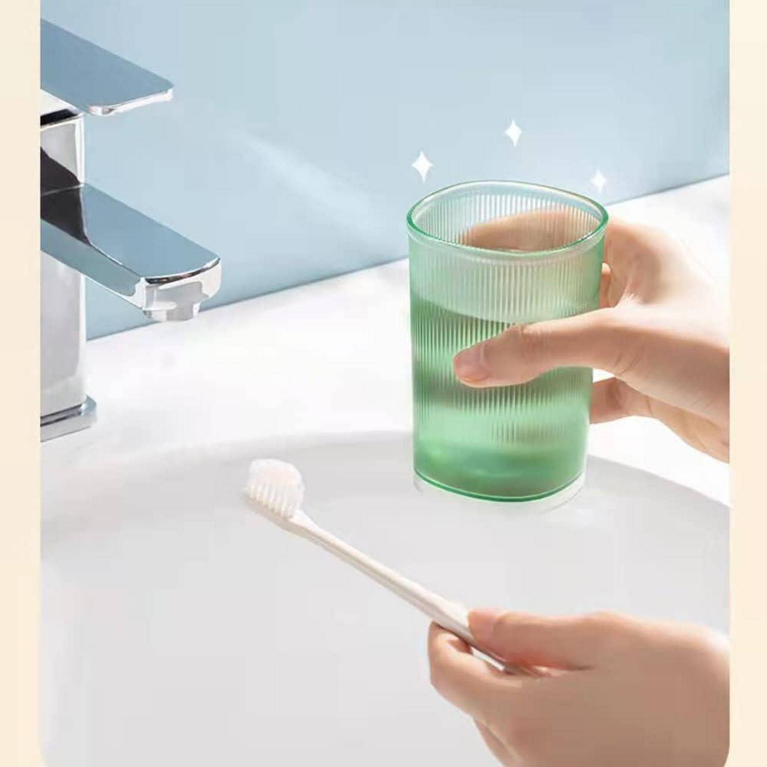 Hände halten einen grünen Zahnbürstenbecher und eine Zahnbürste neben einem Badezimmer-Wasserhahn.