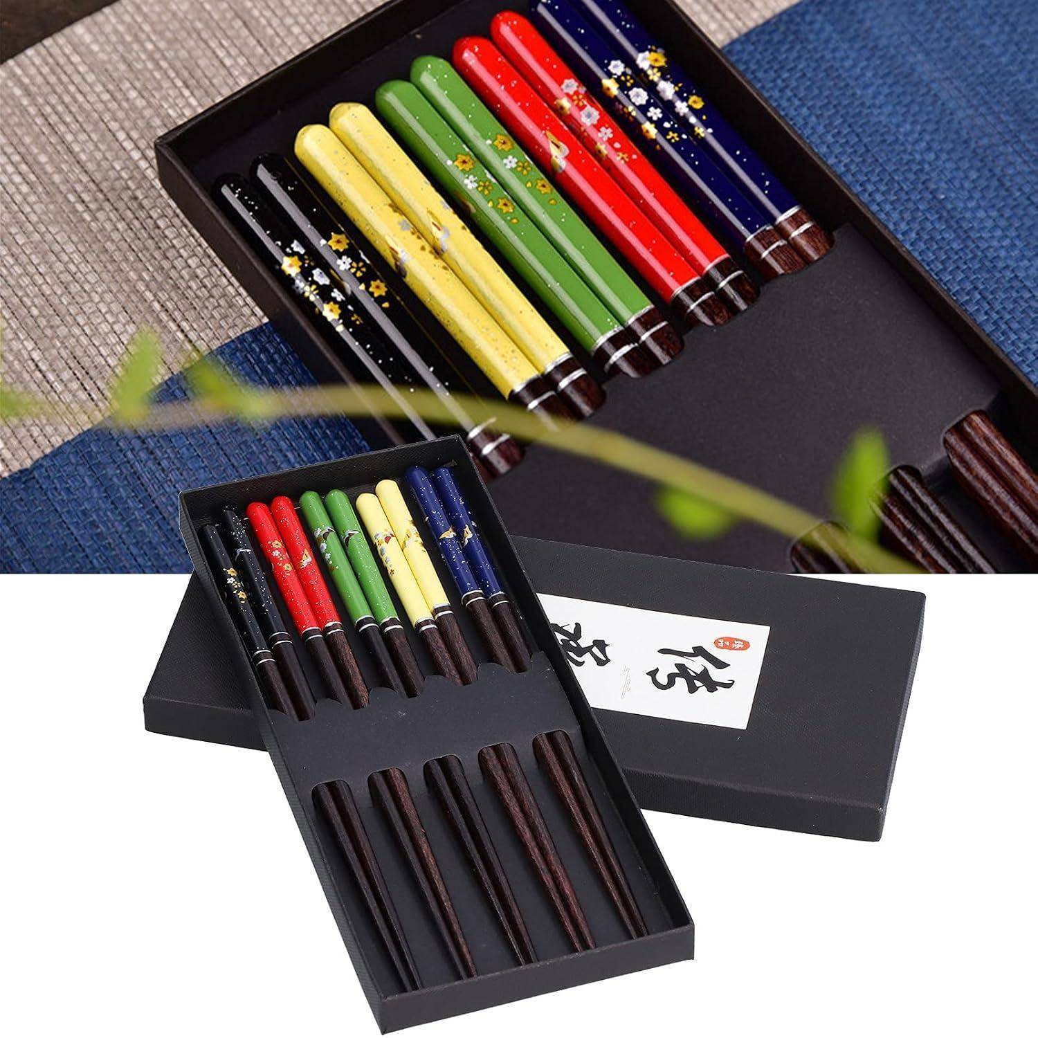 Zwei schwarze Geschenkboxen enthalten farbenfrohe Essstäbchen-Sets in Rot, Gelb, Grün, Blau und Schwarz mit dekorativen Blumenmustern und Holzauflagen.