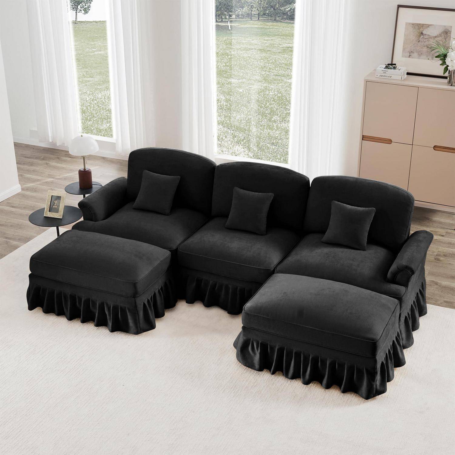Schwarzes modulares Sofa mit drei Rückenkissen, zwei passenden Ottomanen und einem kleinen Beistelltisch in einem hellen Wohnzimmer.